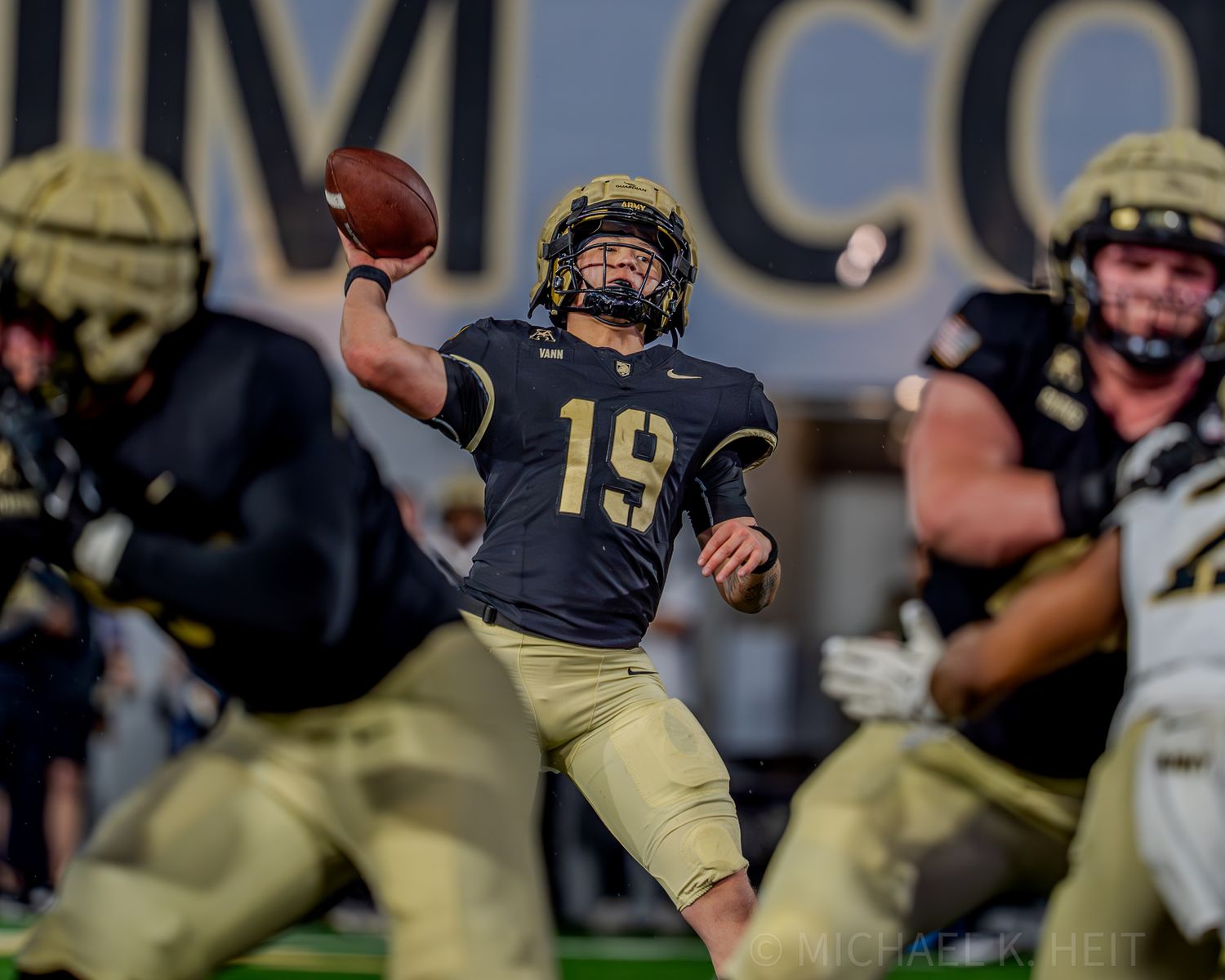 Football players in navy and gold uniforms line up on field during game.