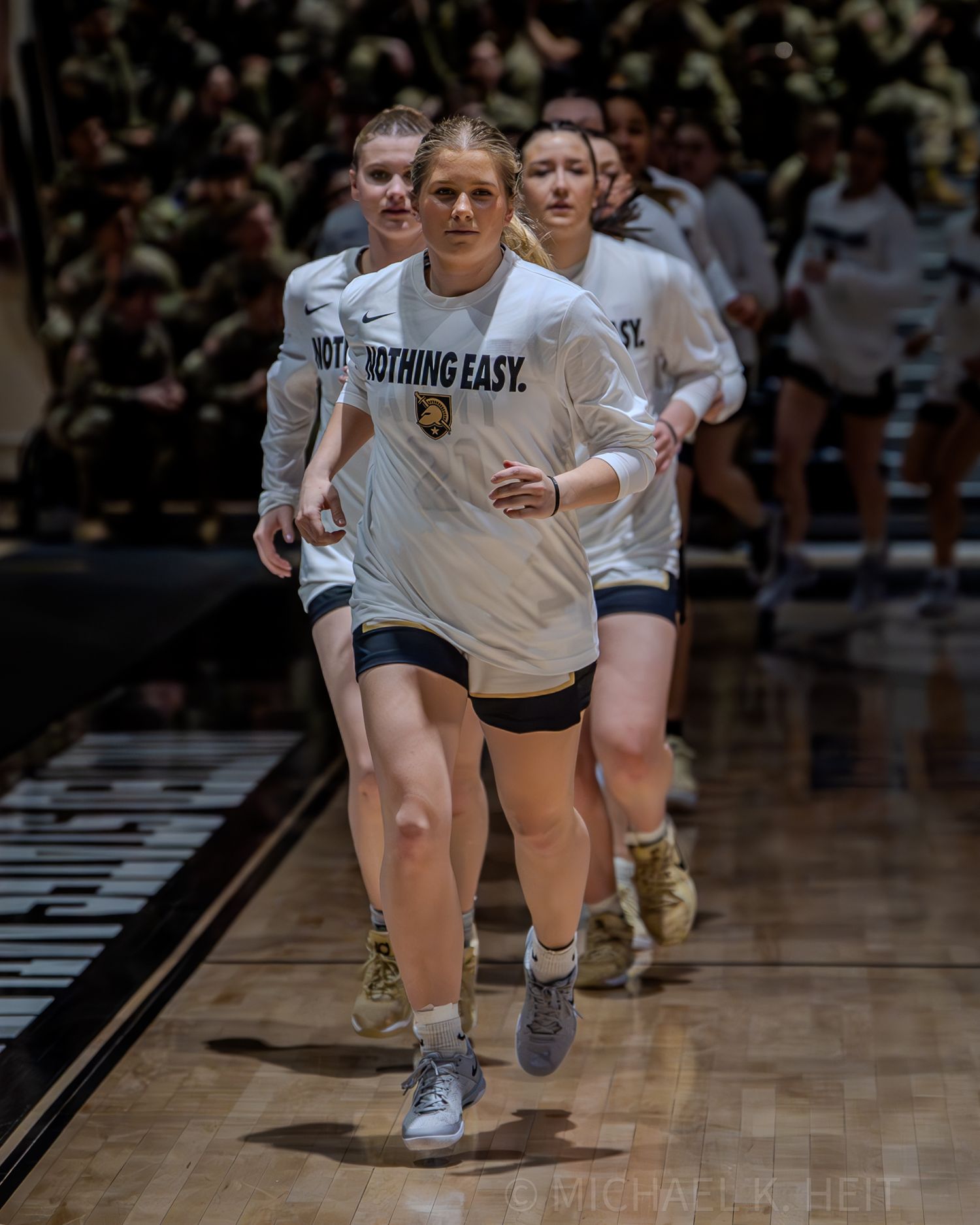 Athletes run across a wooden basketball court during a sporting event.