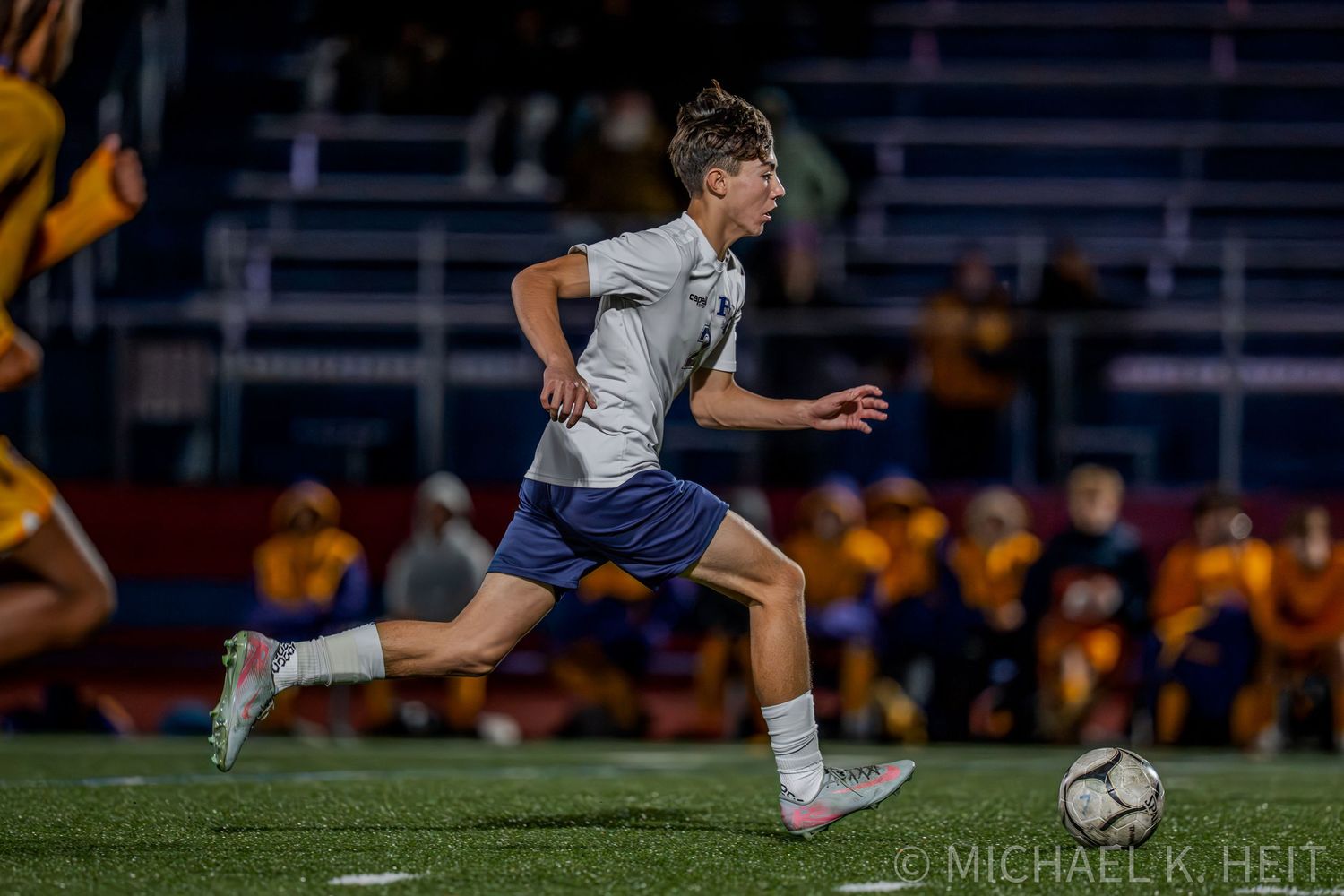 Soccer player stretches low to the ground to make contact with ball during nighttime match.