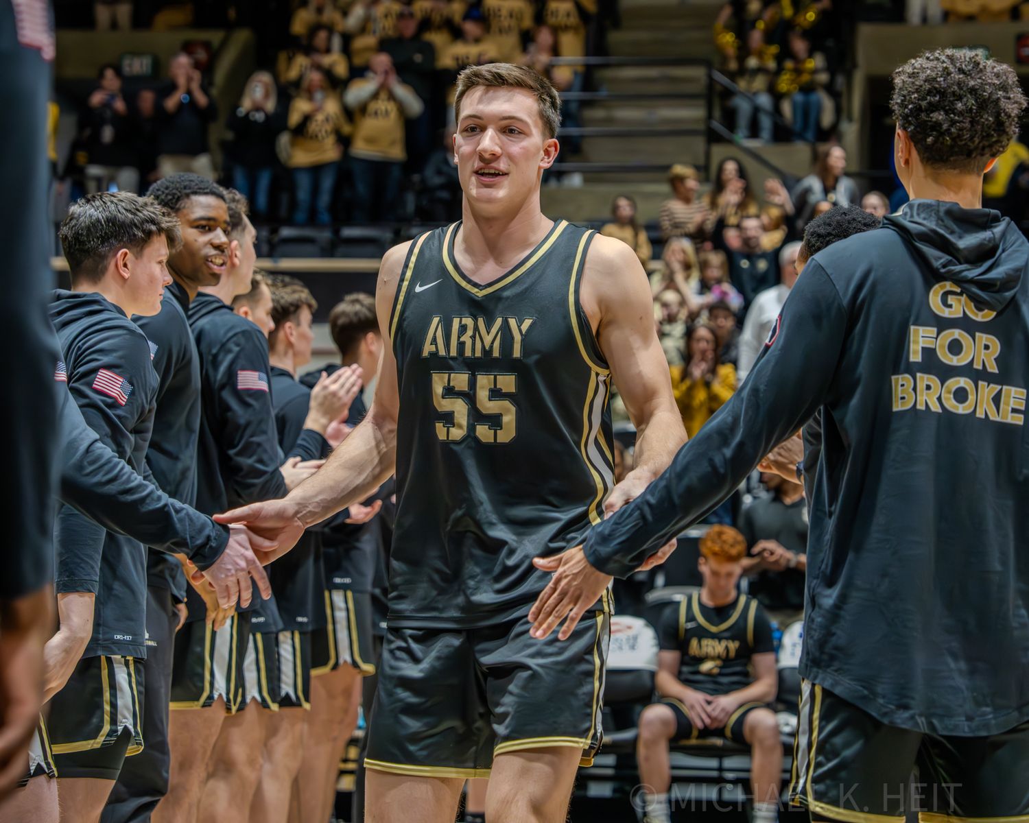 Basketball players in Army uniforms line up during a game with spectators in the background.