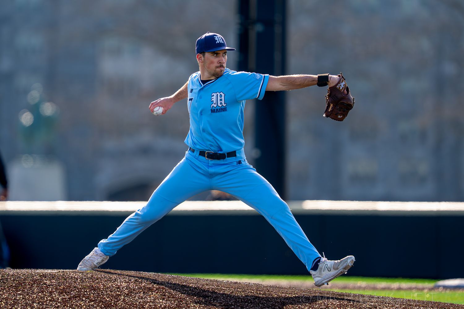 Baseball pitcher in light blue uniform delivers pitch from the mound during game.