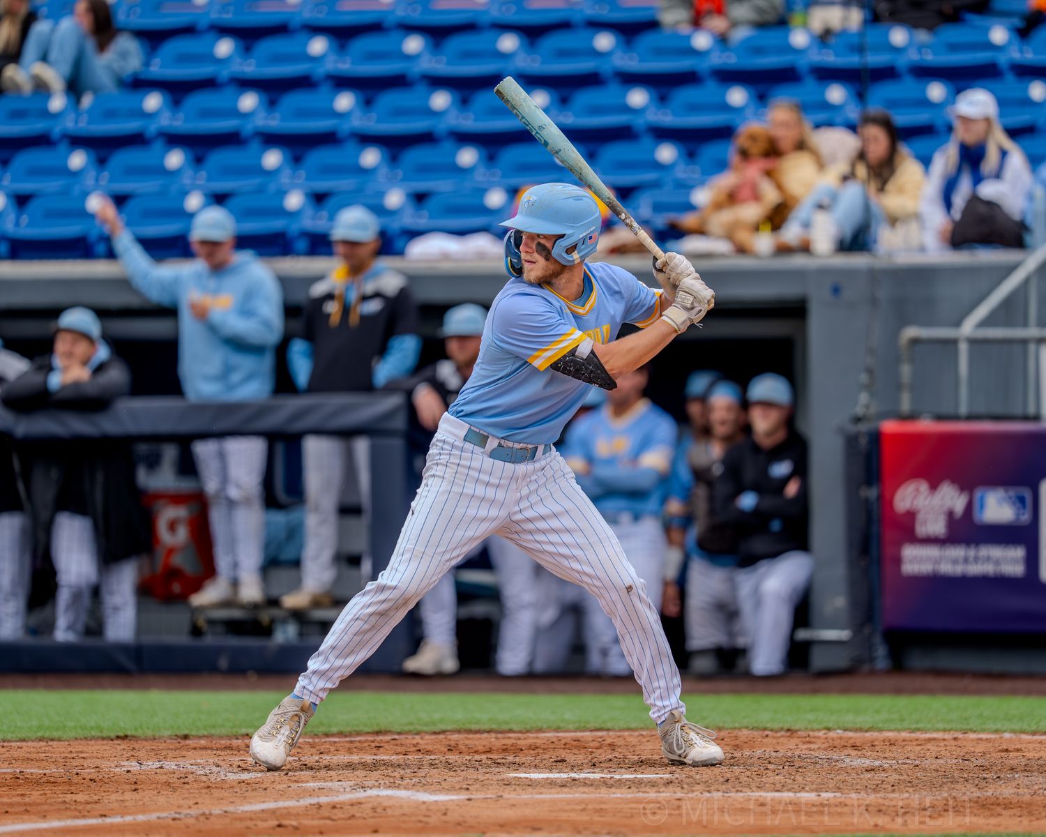 Baseball batter in light blue pinstripe uniform takes stance at home plate during game.