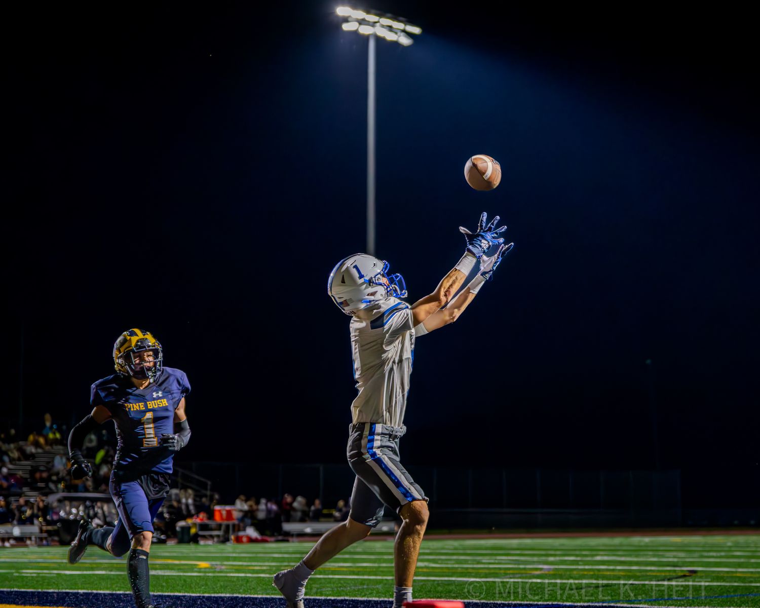 Football soars through night sky during game under stadium lights.