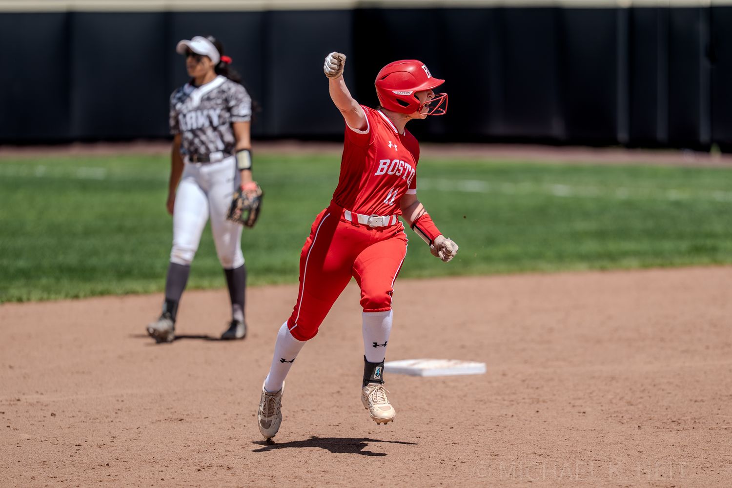 Softball player in red uniform celebrates while running between bases during game.