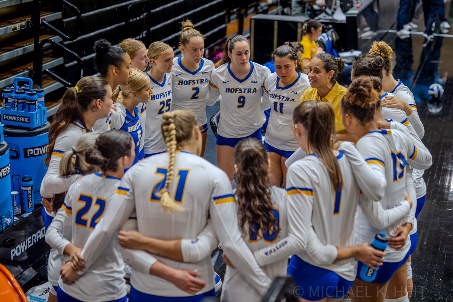 A volleyball team huddles together in blue and white uniforms before a match.