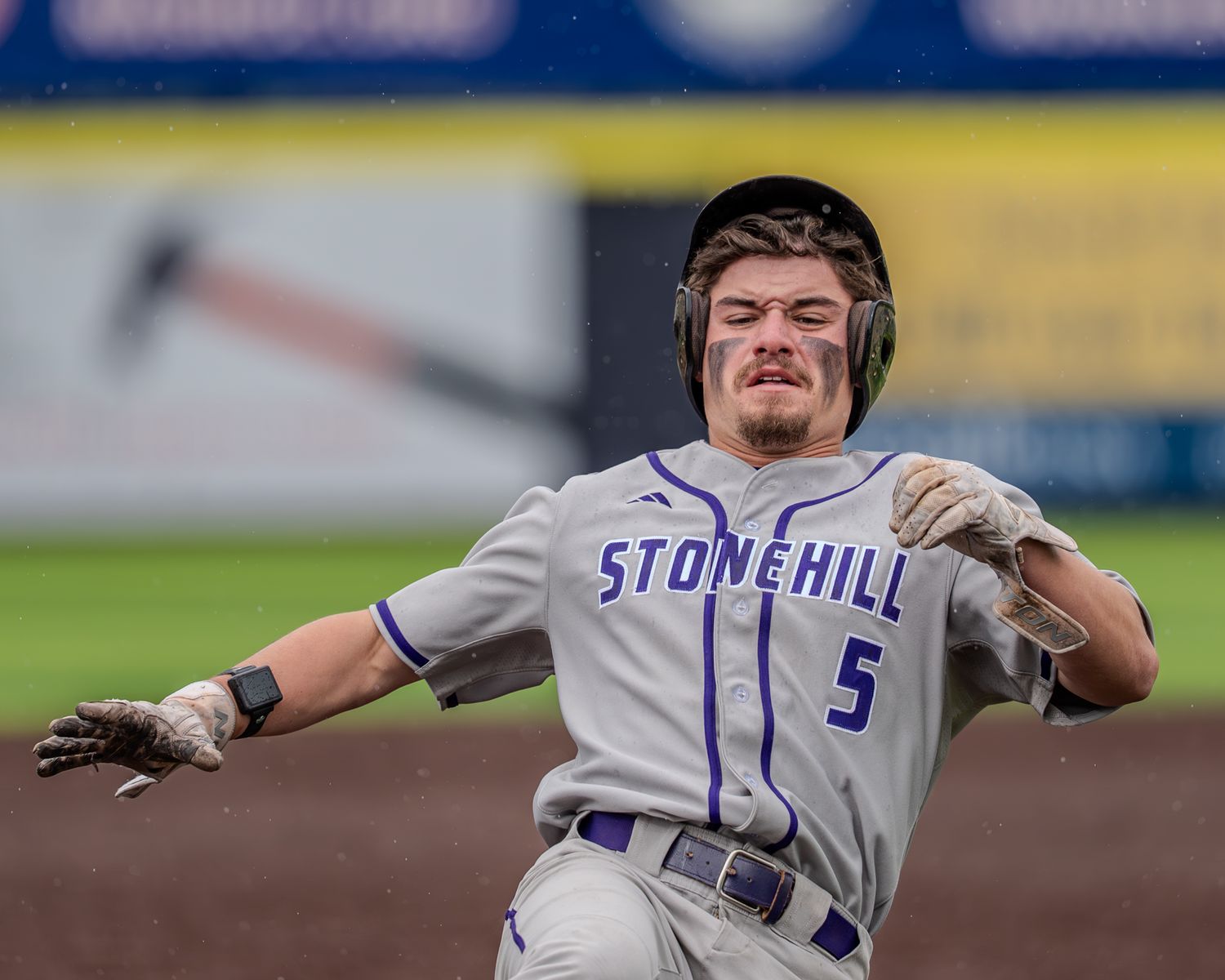 Baseball player in gray uniform with blue lettering swings bat during game at outdoor stadium.