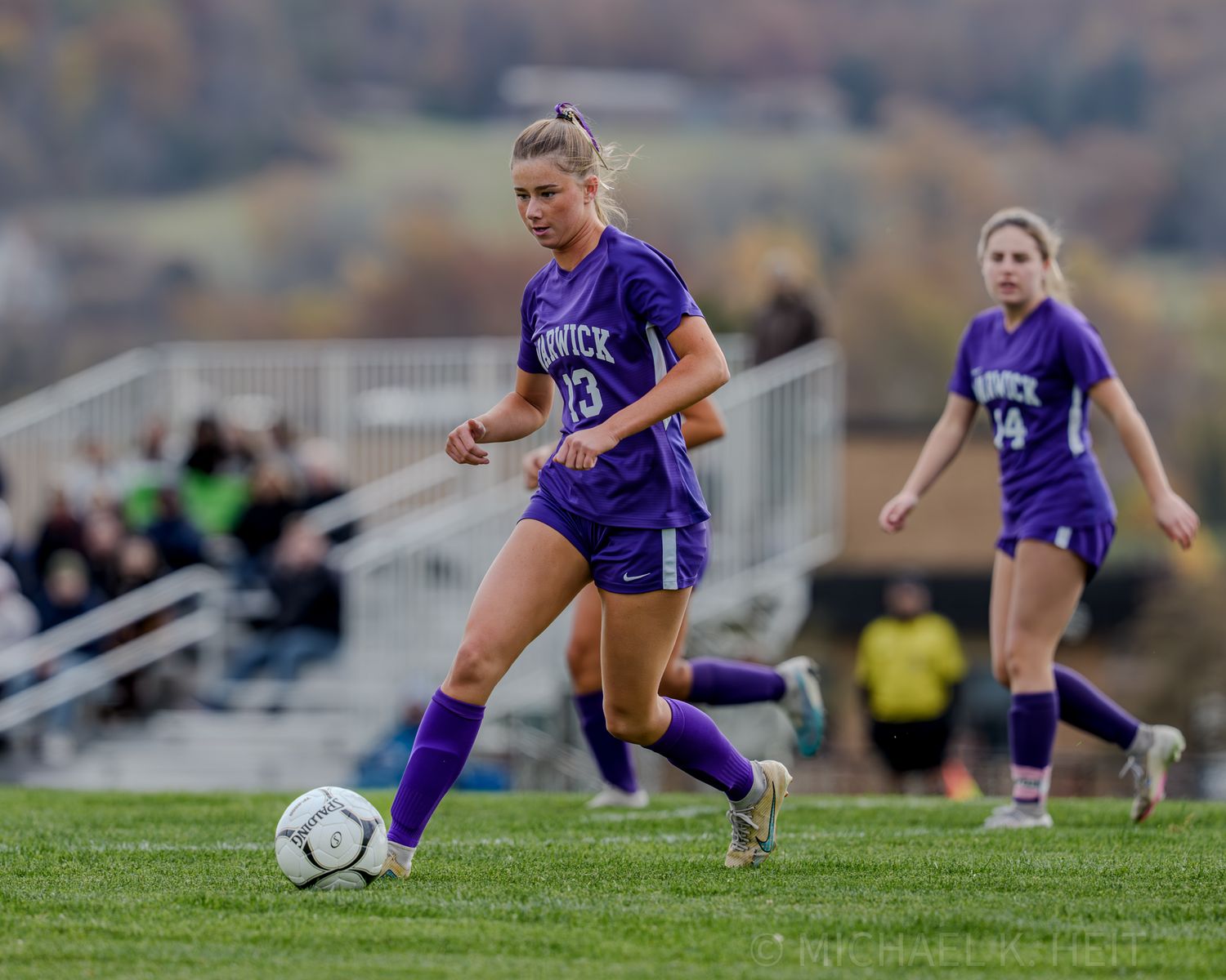 Soccer player in purple jersey executes sliding tackle during competitive match on grass field.