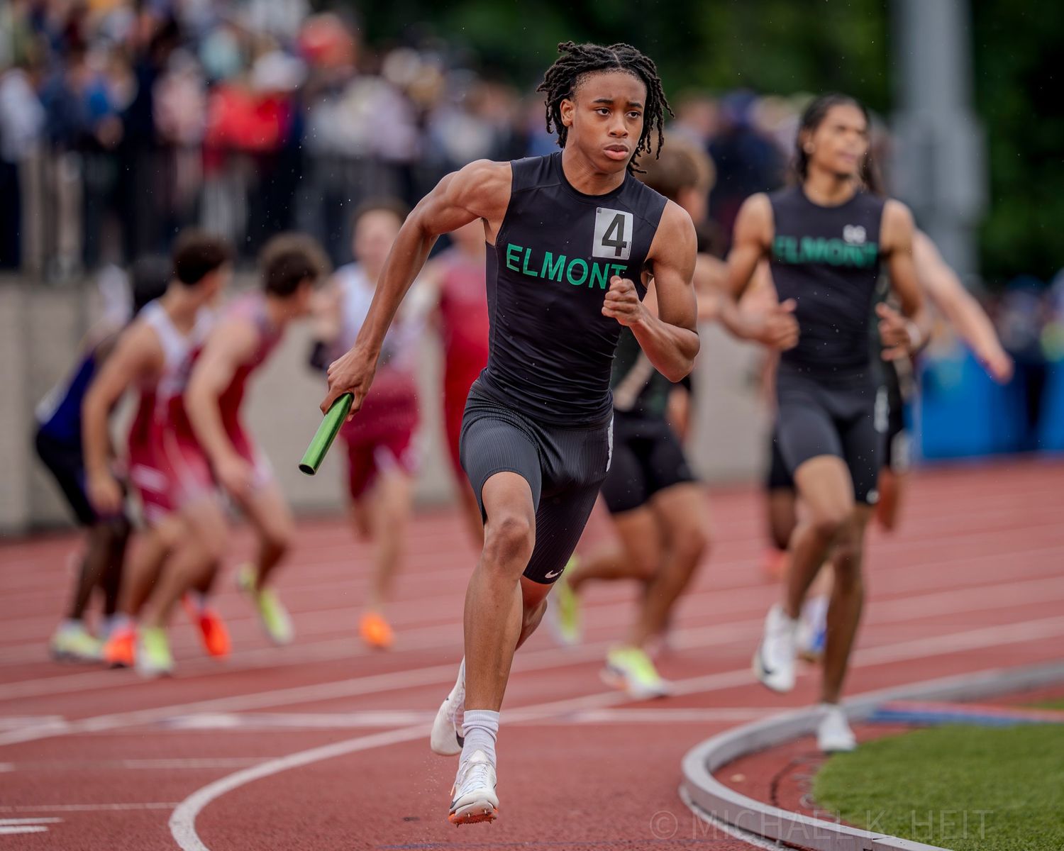 Runners compete in a high-stakes track meet on a sunny day.