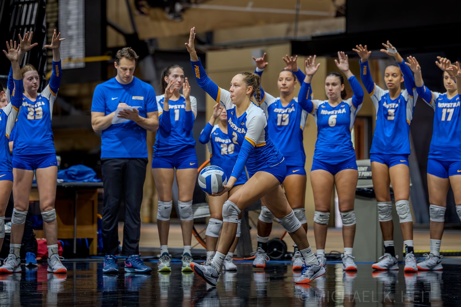 Volleyball team in blue uniforms lined up on the sideline during a match.