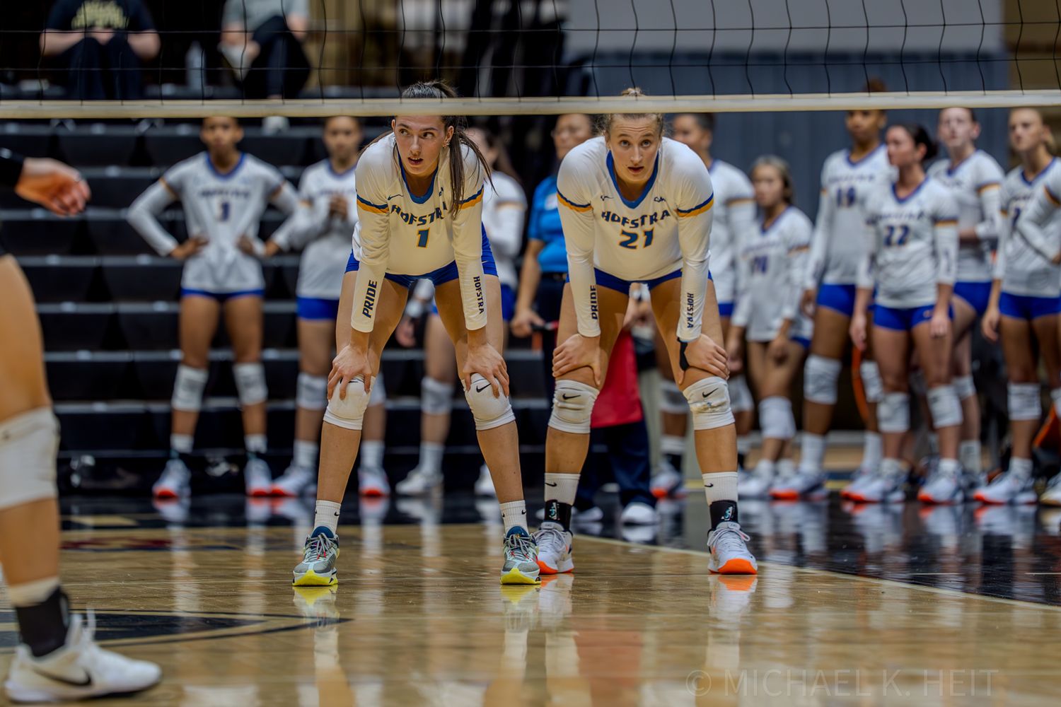 Two volleyball players crouch in ready position awaiting the serve.