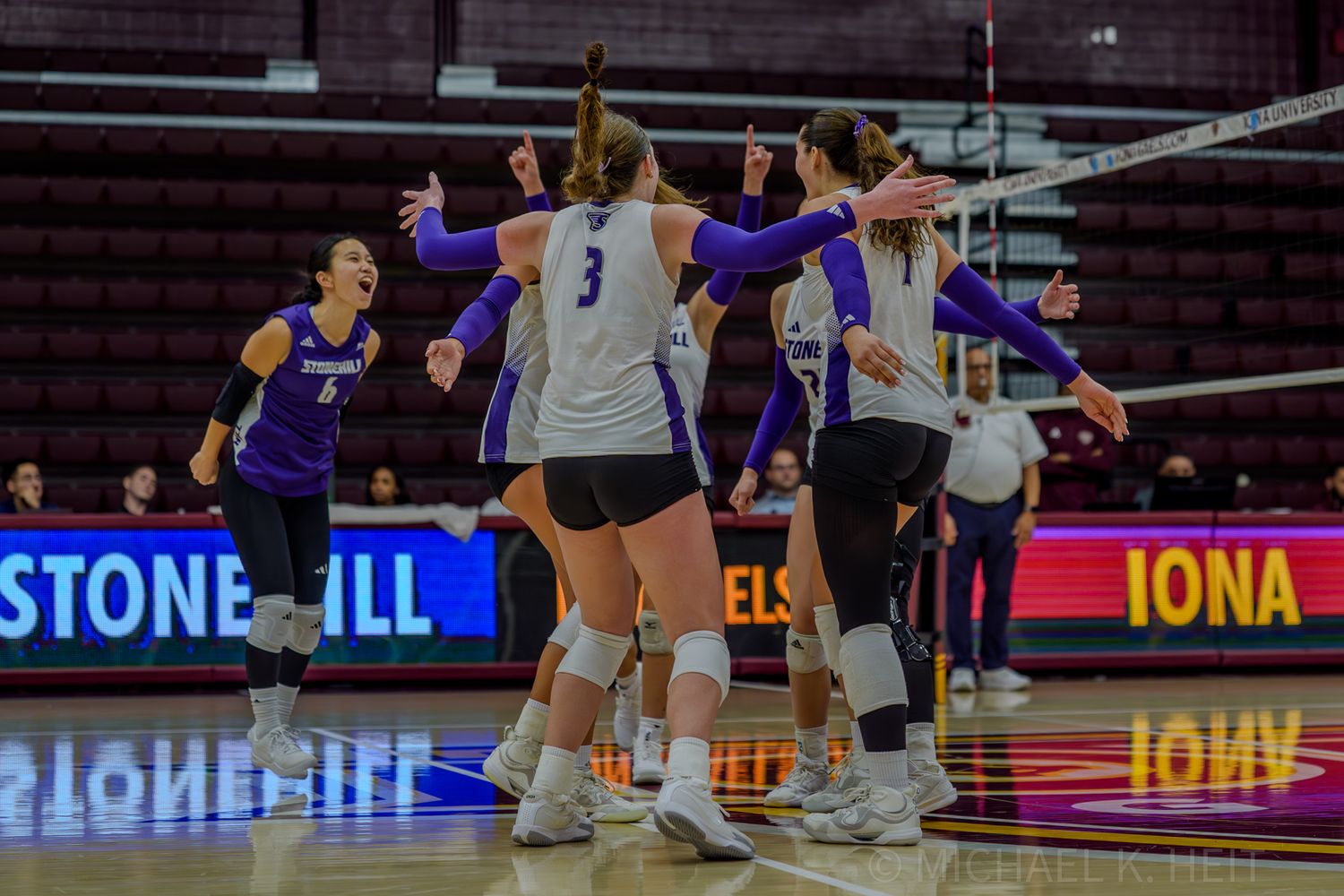 Volleyball teams face off during a competitive indoor match with scoreboard visible in background.