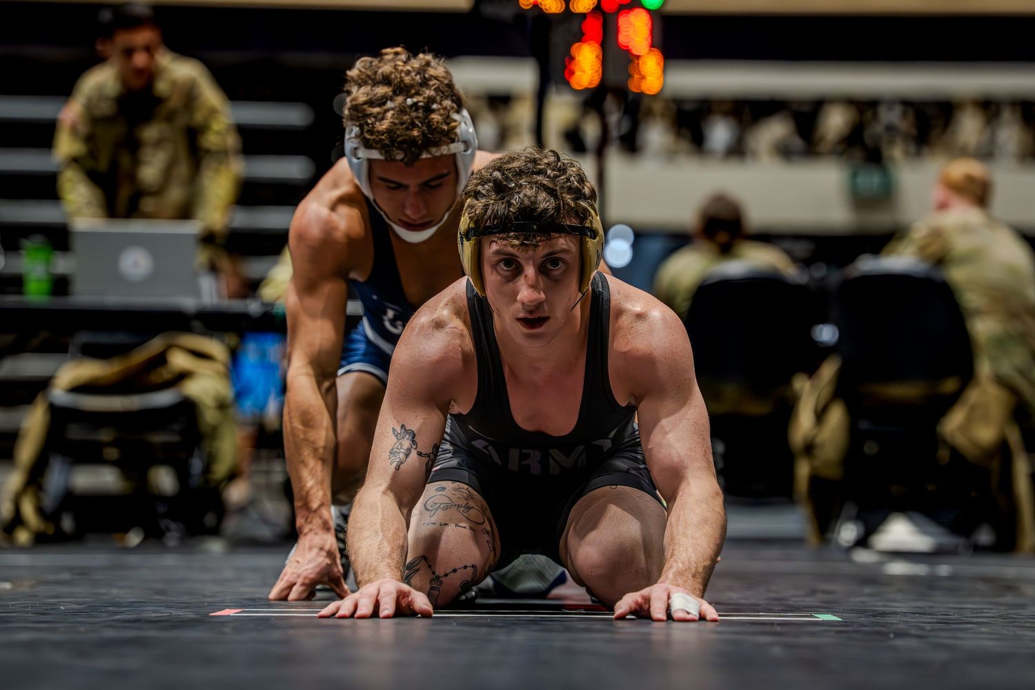 Two wrestlers compete on a mat, one wearing an Army singlet, during an intense wrestling match.