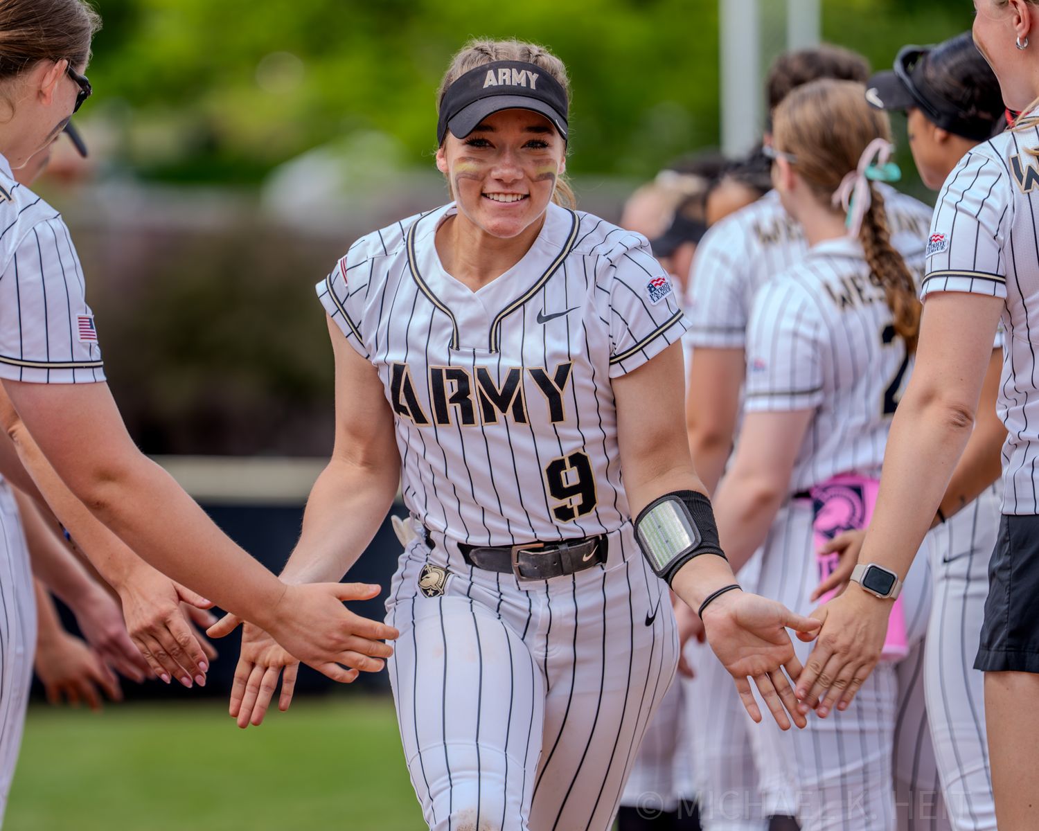 Army softball team members in pinstripe uniforms share high fives in dugout area.
