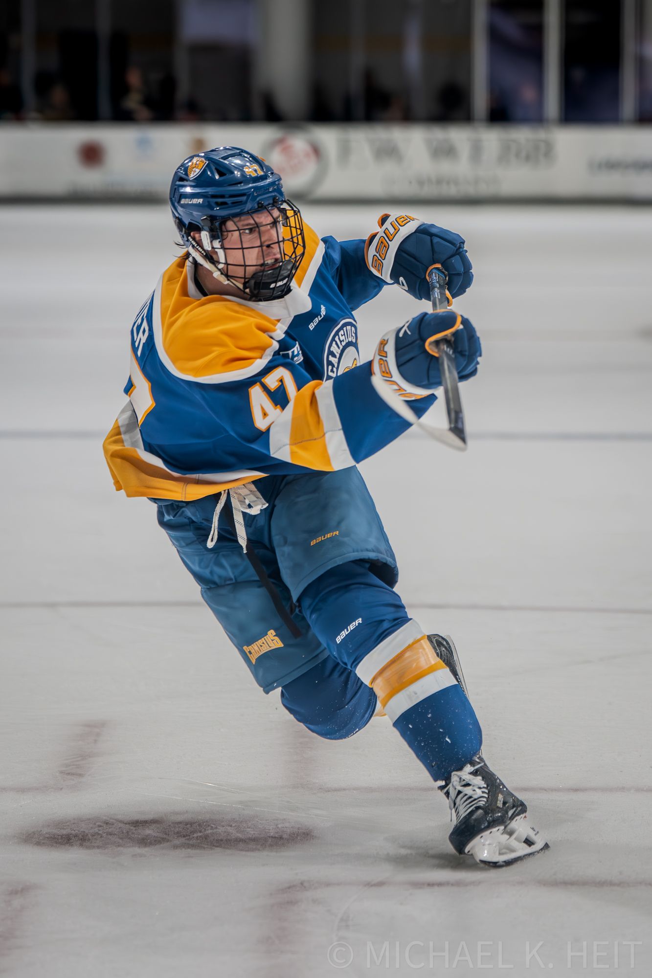 Ice hockey player in blue and gold uniform executes sharp turn while skating at high speed.