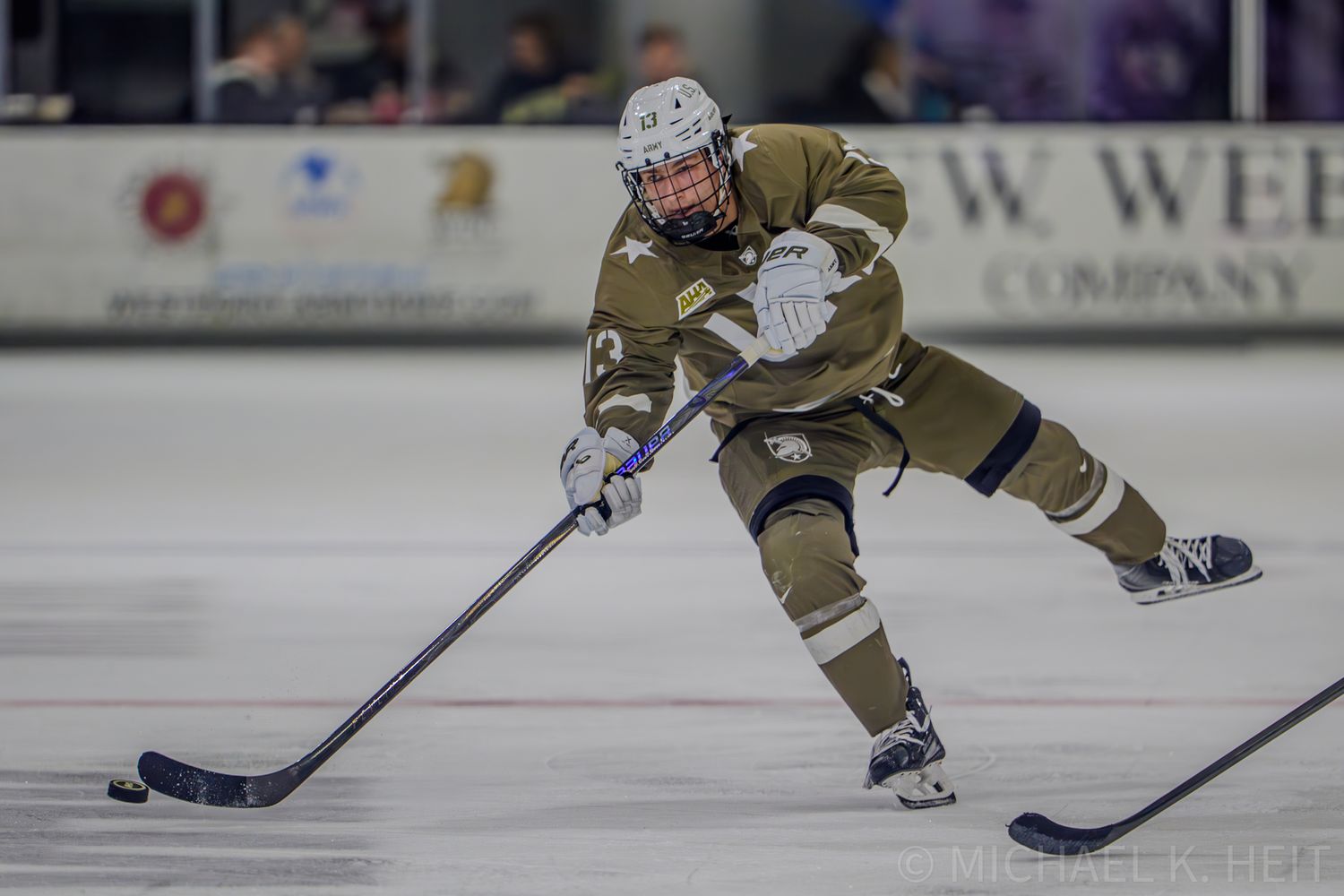 Hockey players in tan uniforms chase the puck during competitive ice match.