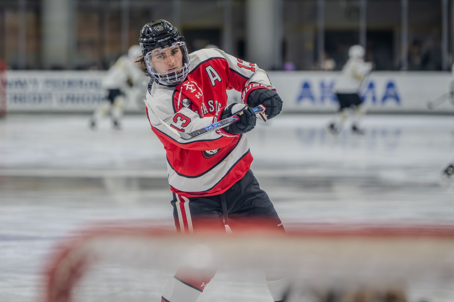A hockey player in red and white jersey takes a shot during an ice hockey game.