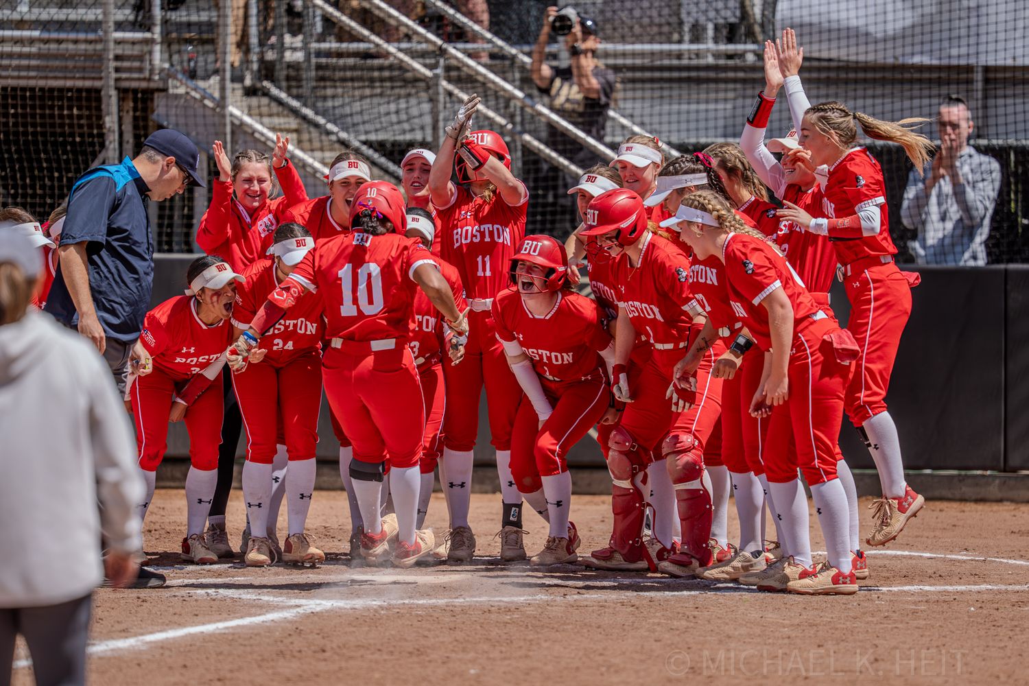 Team in red uniforms celebrates together at home plate during softball game.