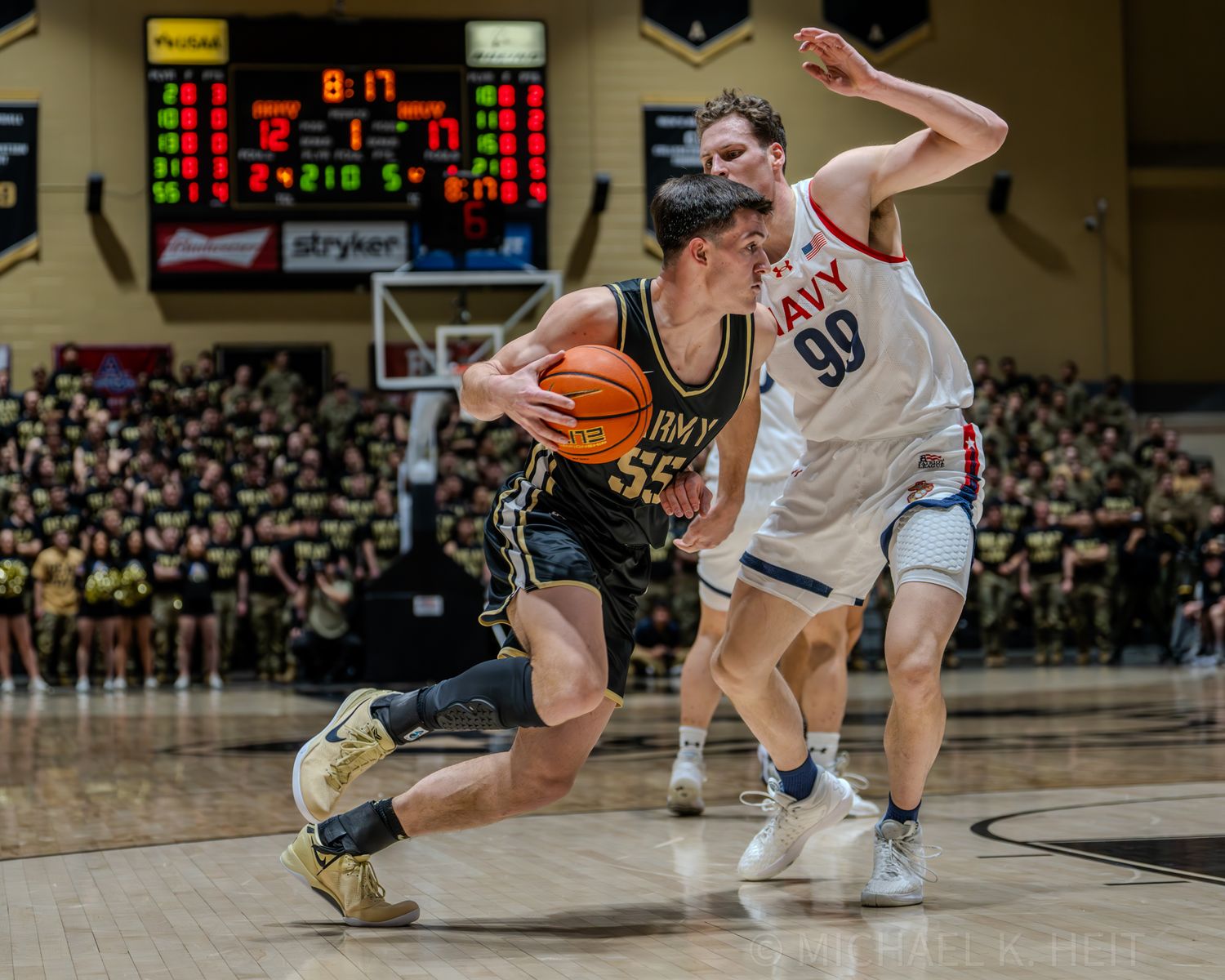 Basketball players move across the court during a competitive game with scoreboard visible.
