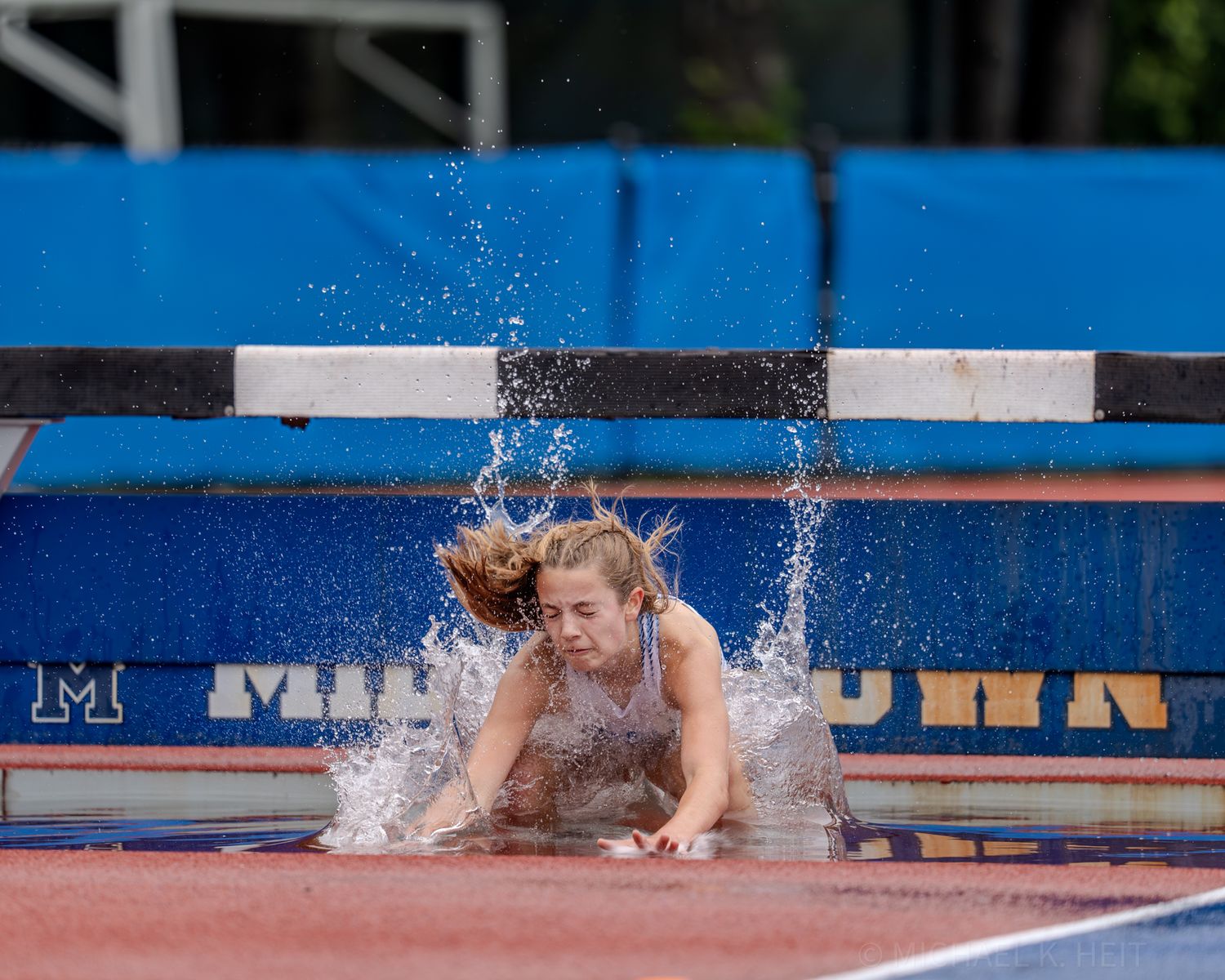 A person splashes into water while diving across a blue athletic mat during a sporting event.