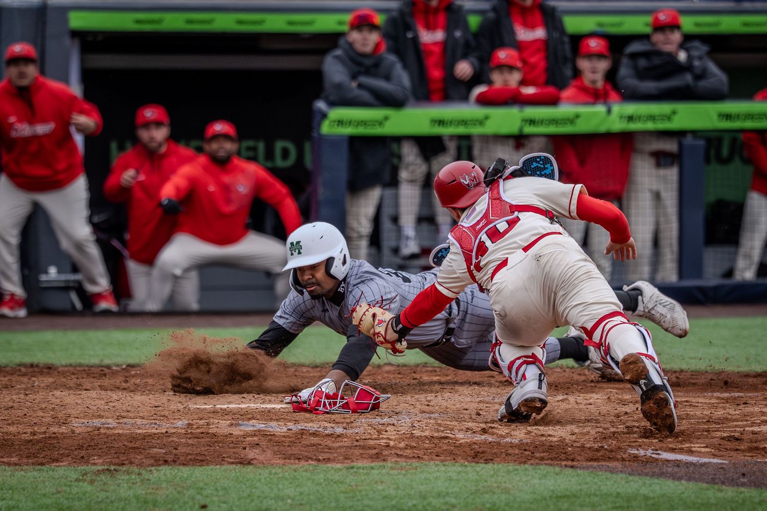Baseball player in red uniform slides into home plate during game action sequence.