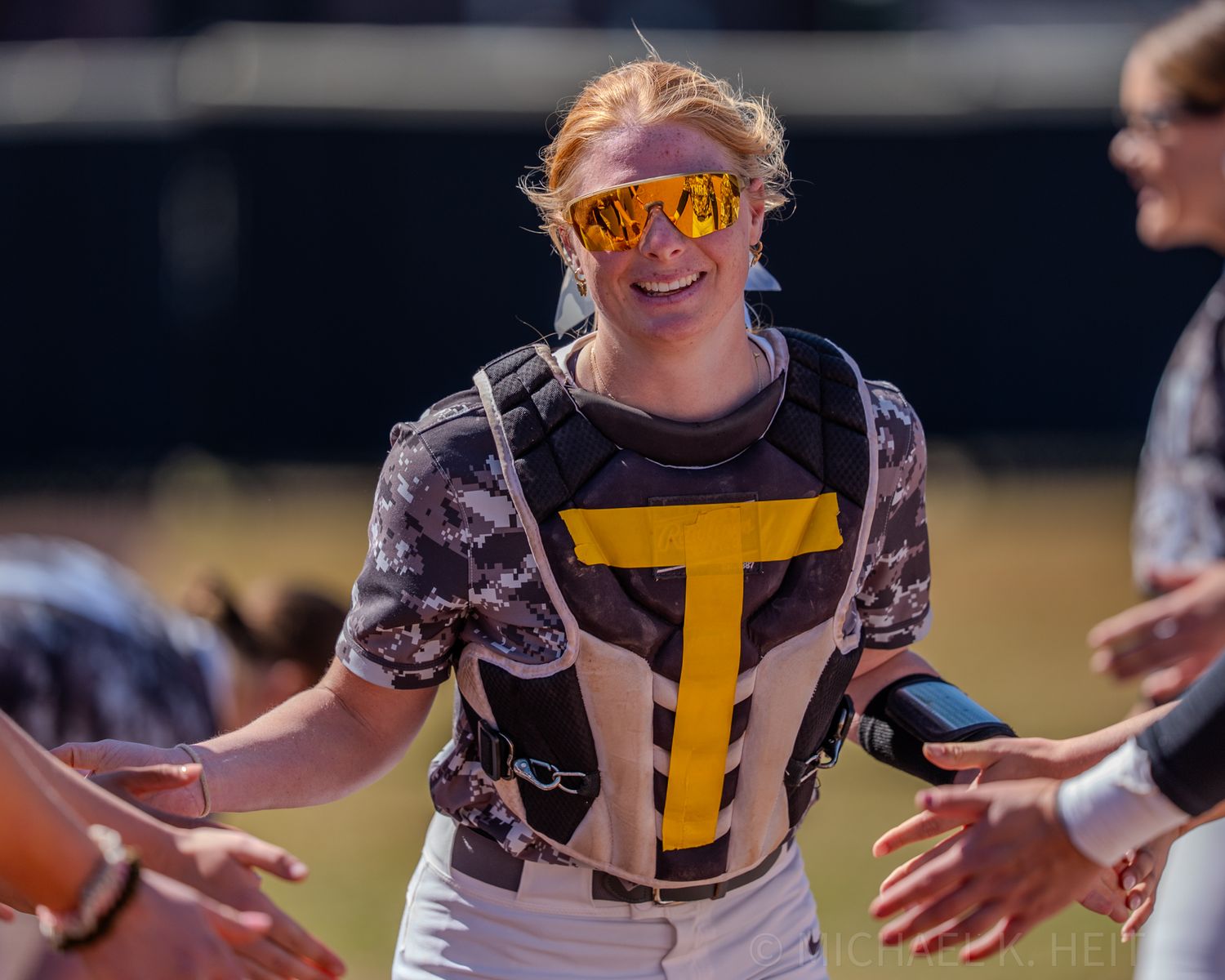 Player in tie-dye shirt and yellow sunglasses celebrates during softball game.