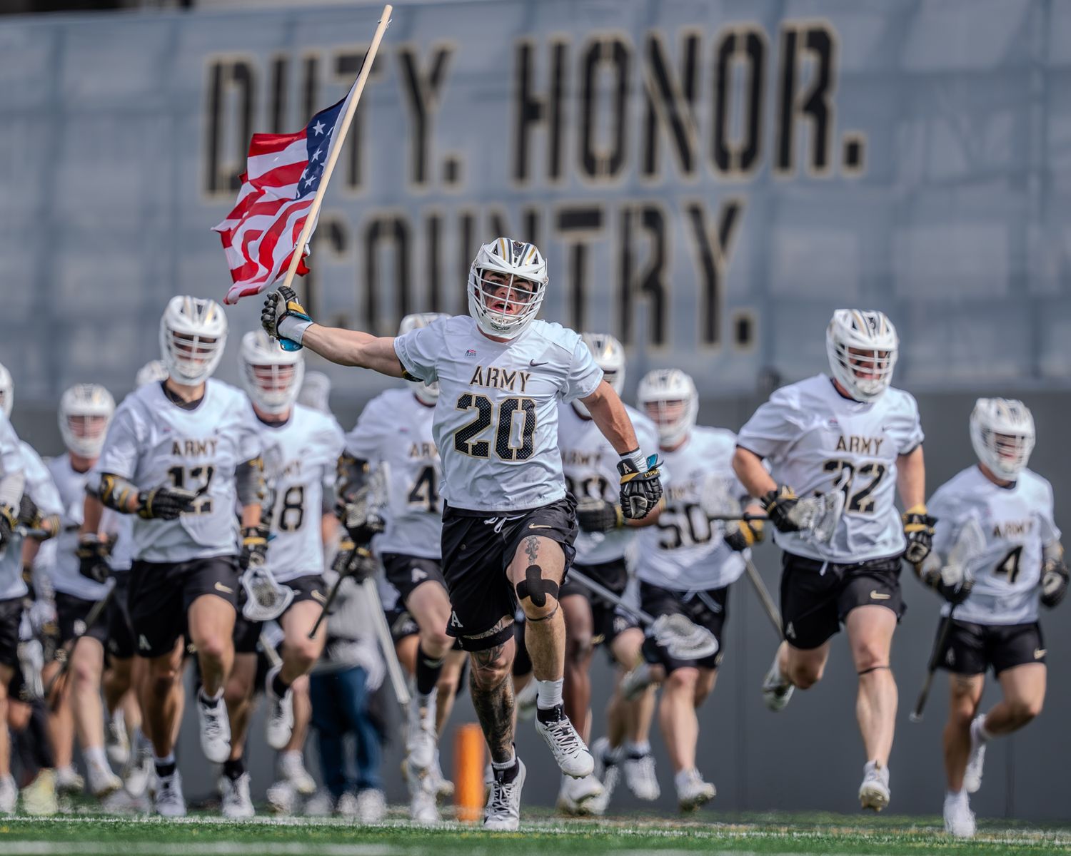 Wide shot of lacrosse game showing multiple players in action on the field.