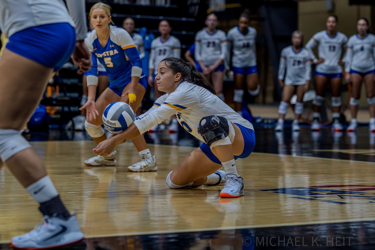 Players in blue and white uniforms position themselves for a play during volleyball match.