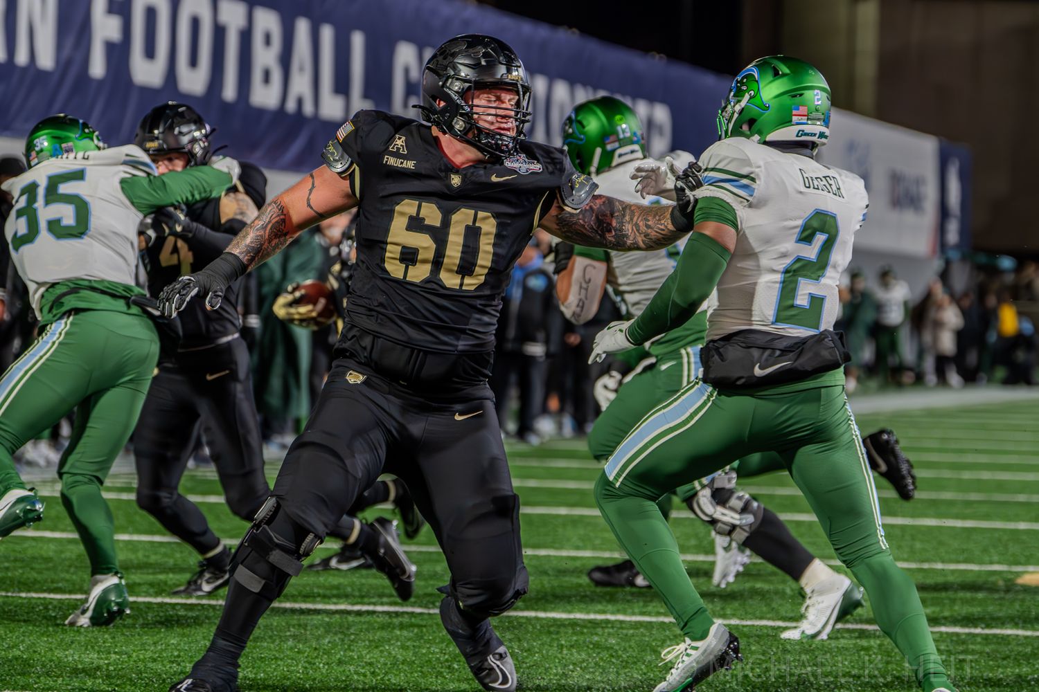Football players in green and black uniforms line up for a play during a competitive match.