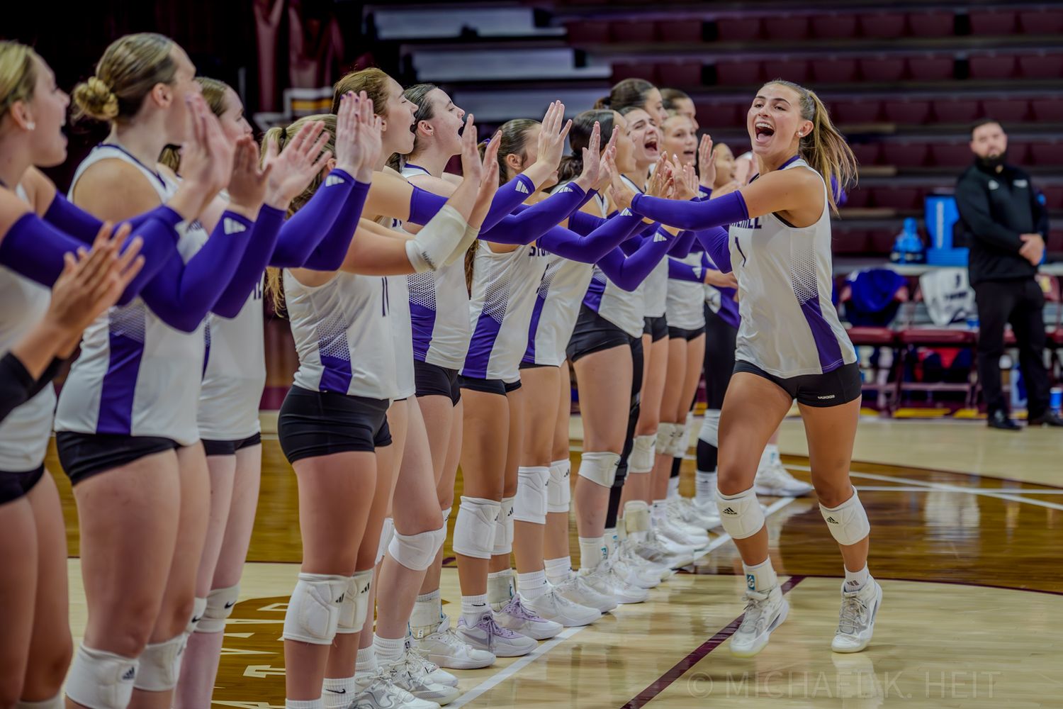 Volleyball team lines up on the court in purple and white uniforms before a match.