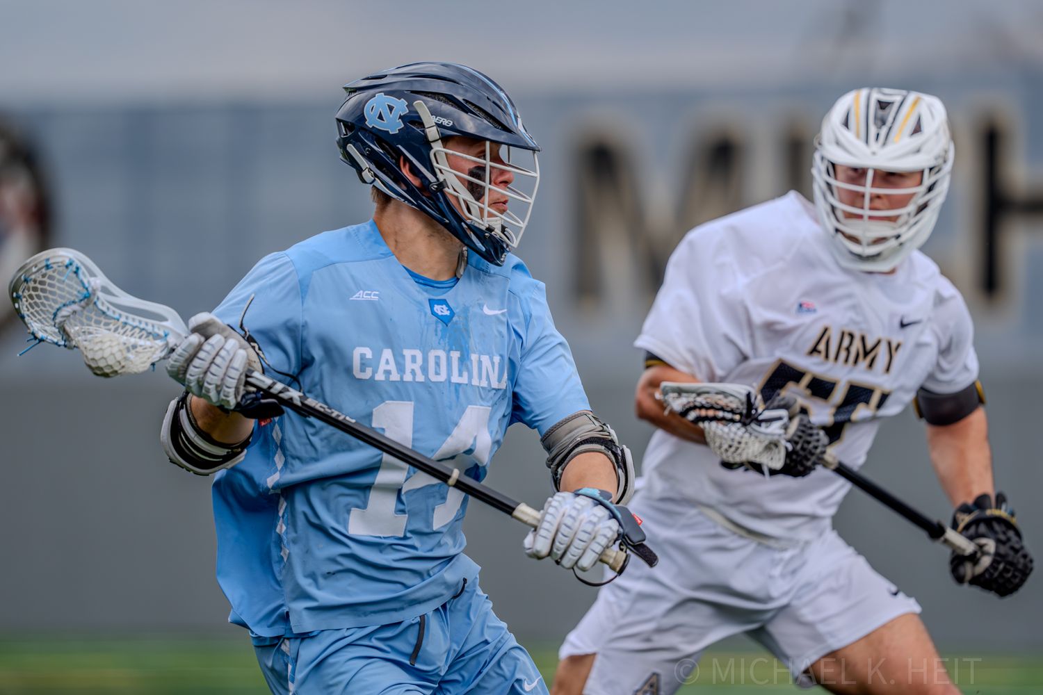 Lacrosse players from opposing teams engage in a ground battle for the ball.