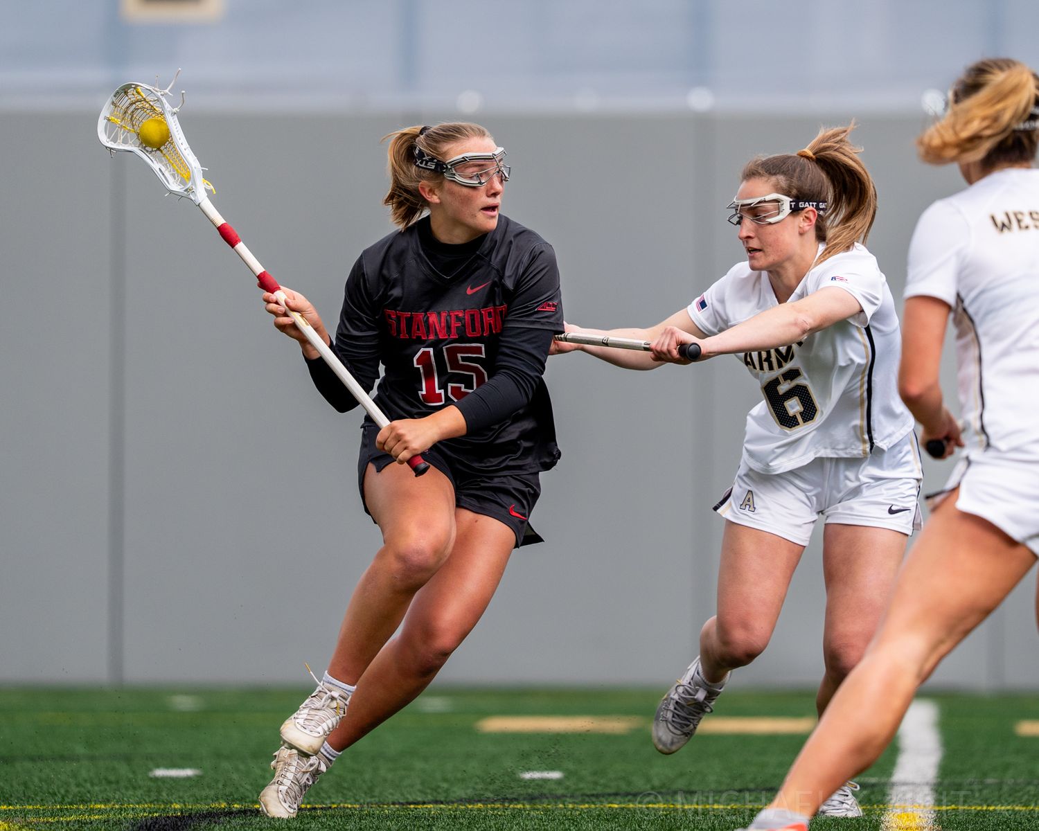 Players dive and stretch for a loose ball during a women's college lacrosse game.