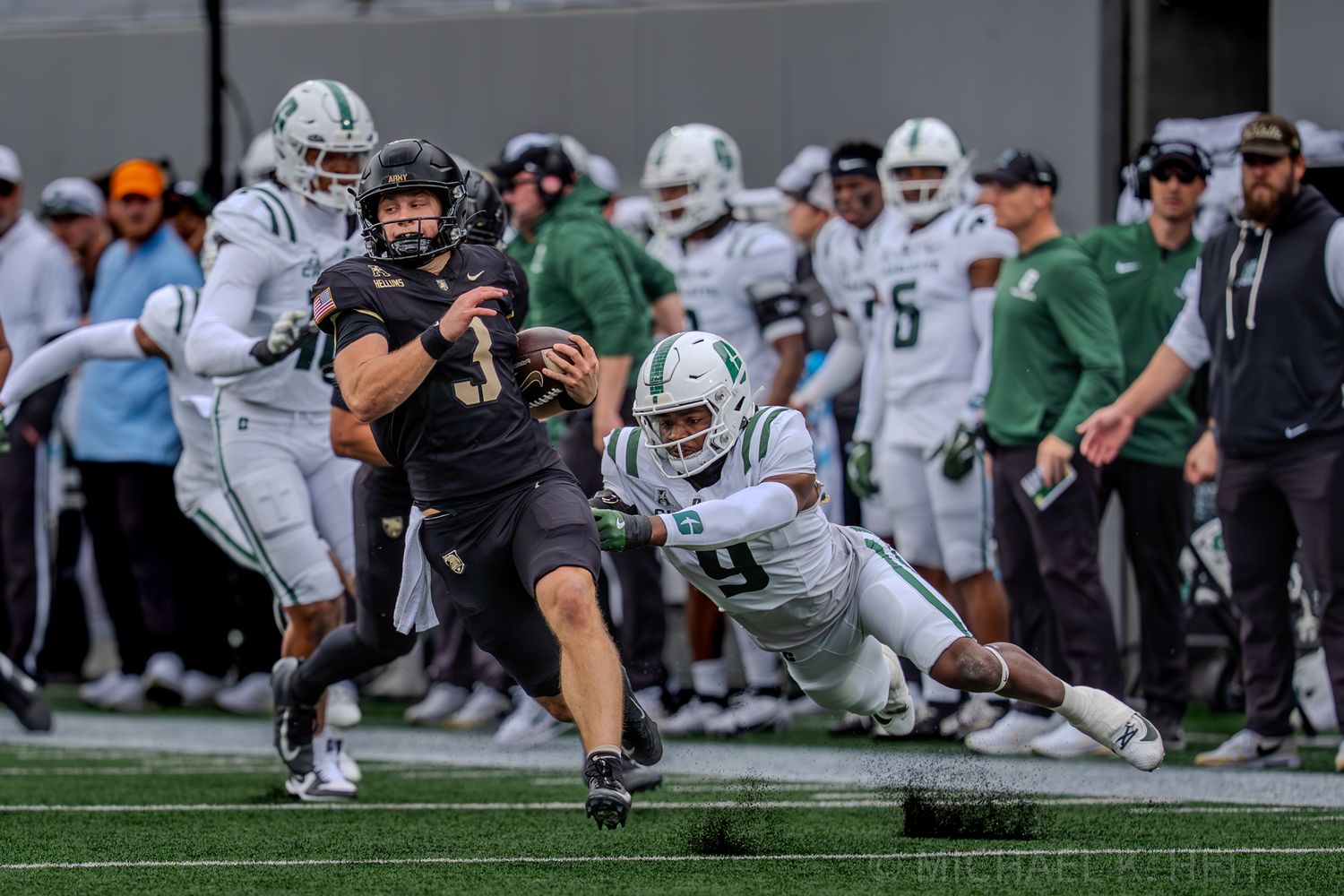 Football player in black uniform attempts to catch the ball during an intense game play.