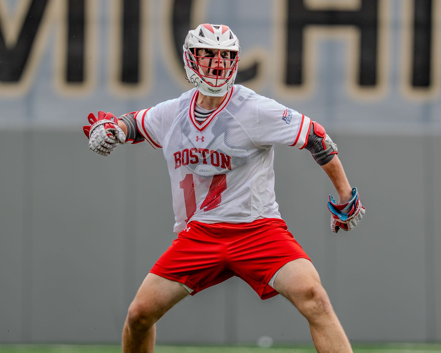 Lacrosse players in white and maroon uniforms position themselves during competitive play.