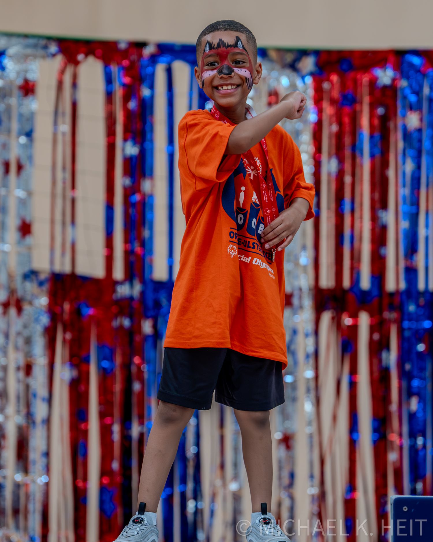 Young participant celebrates at Special Olympics event with patriotic red white and blue decorations.