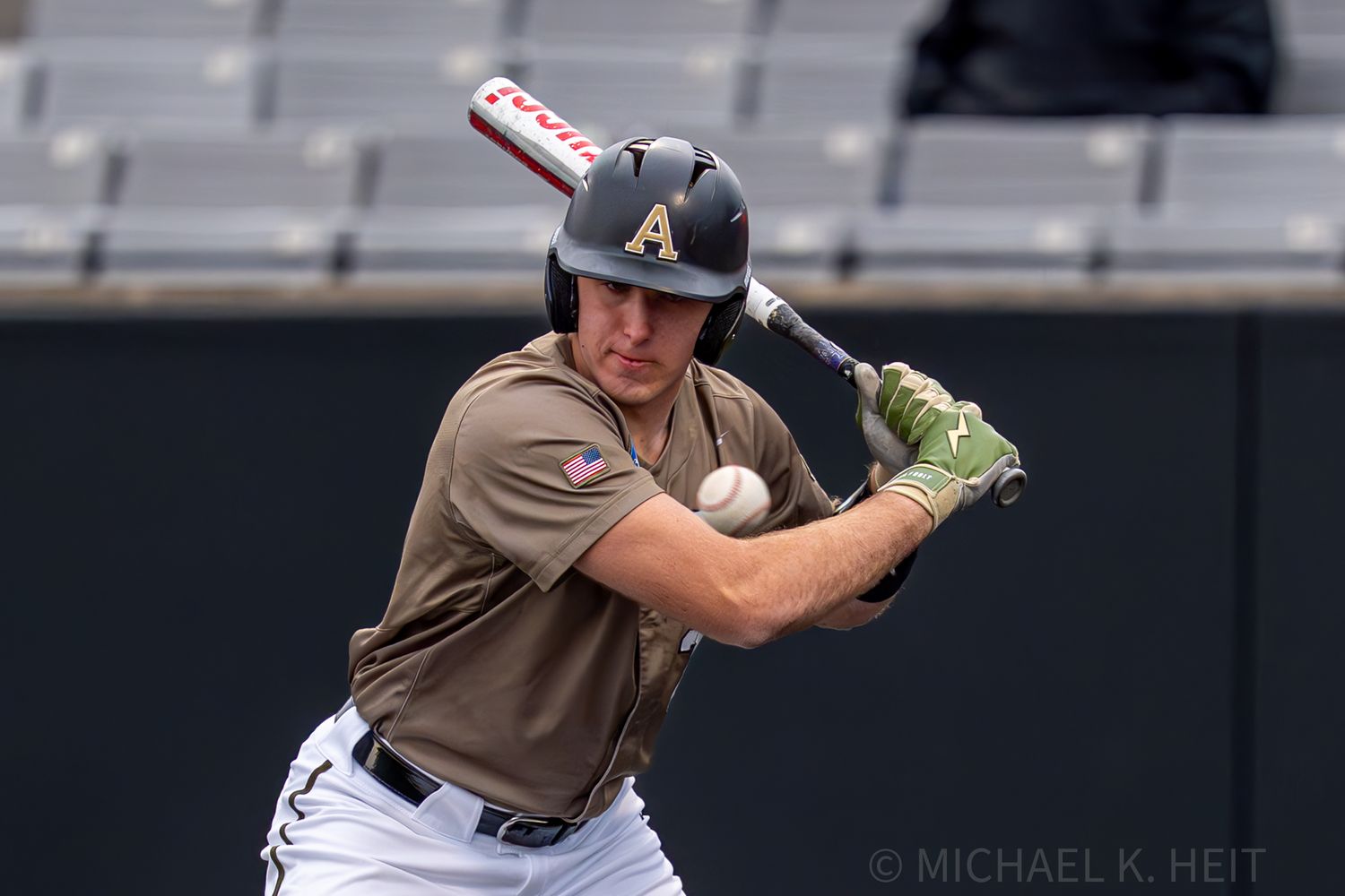 Baseball player in tan uniform follows through on swing during game on field.