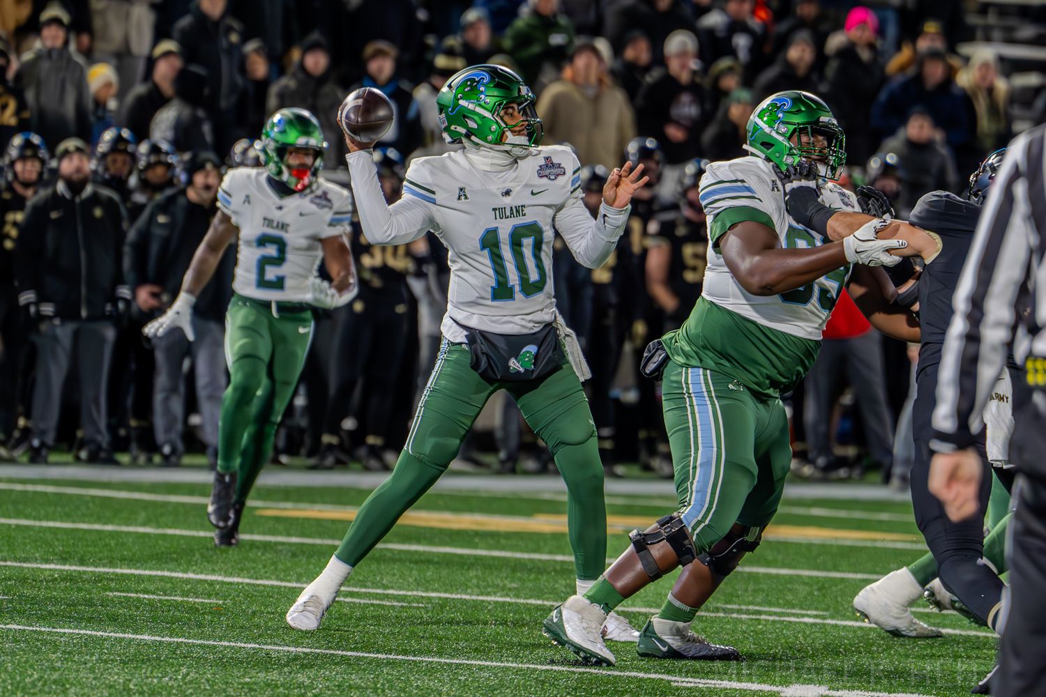 Football players in green and white uniforms compete on field during night game.