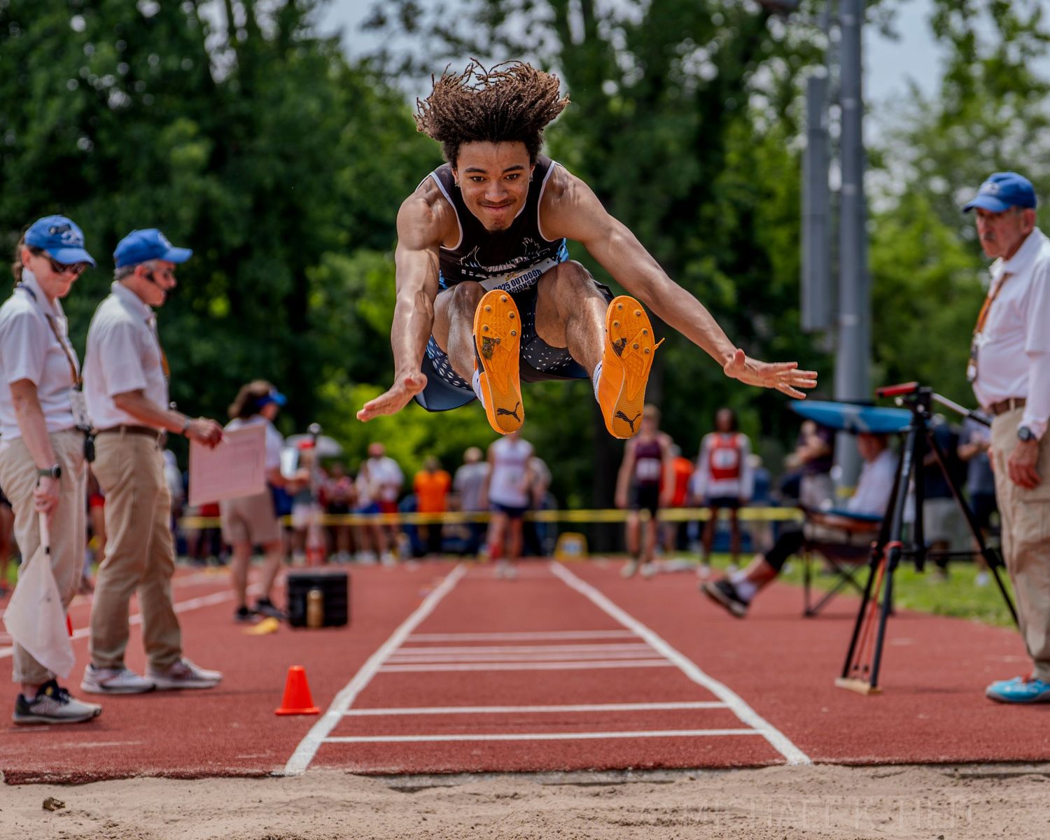 Athletes compete in long jump during a track and field meet with sand pit landing.