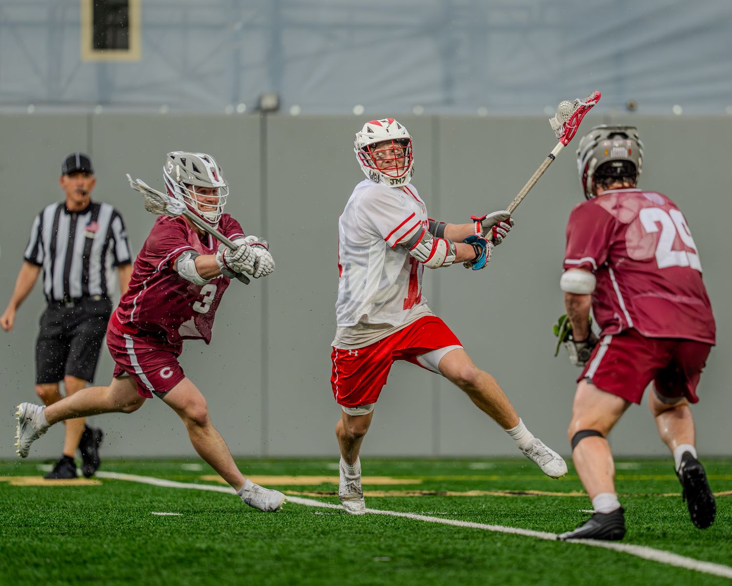 Lacrosse players dive and stretch for the ball during an athletic play on the turf field.