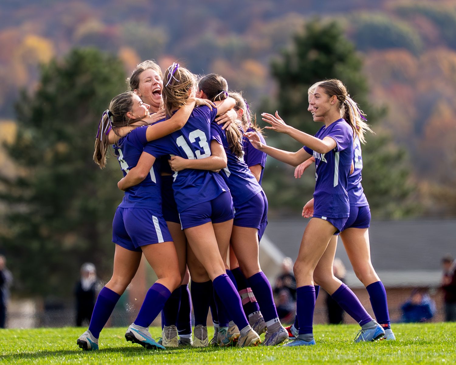 Women's soccer team players in blue uniforms sitting on grass field during autumn season.