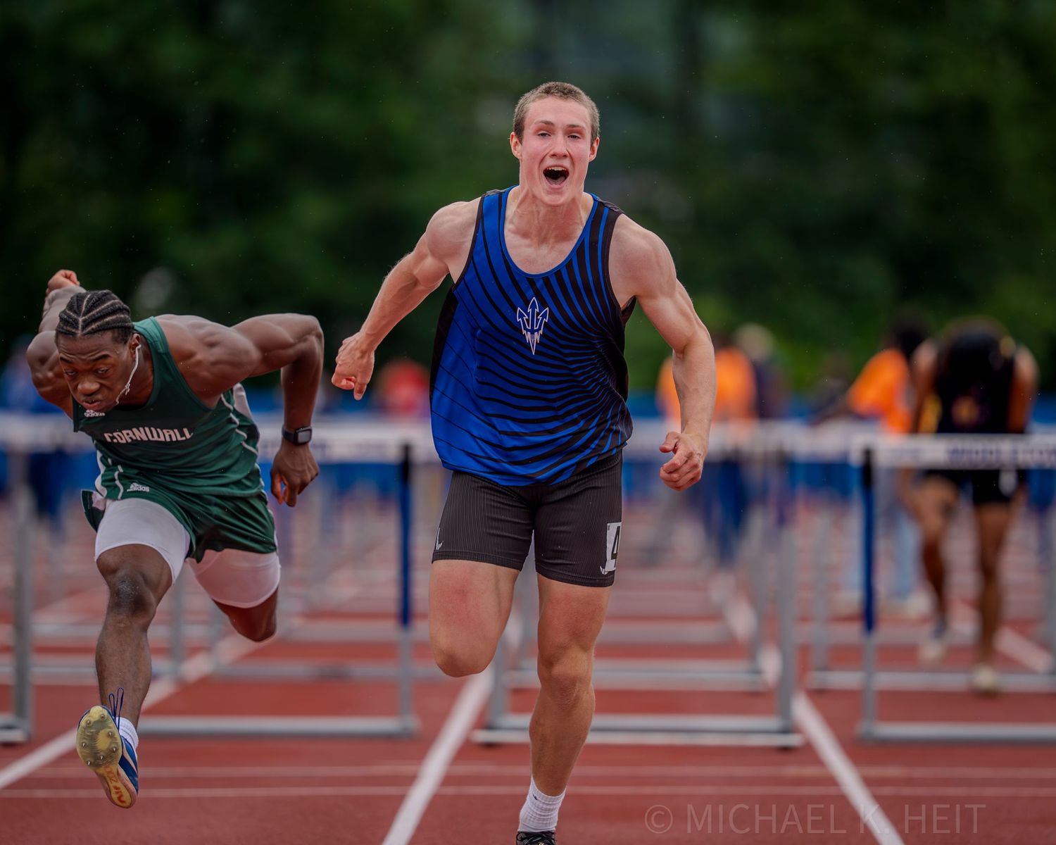 Track athletes clear hurdles in synchronized motion during an outdoor competition.