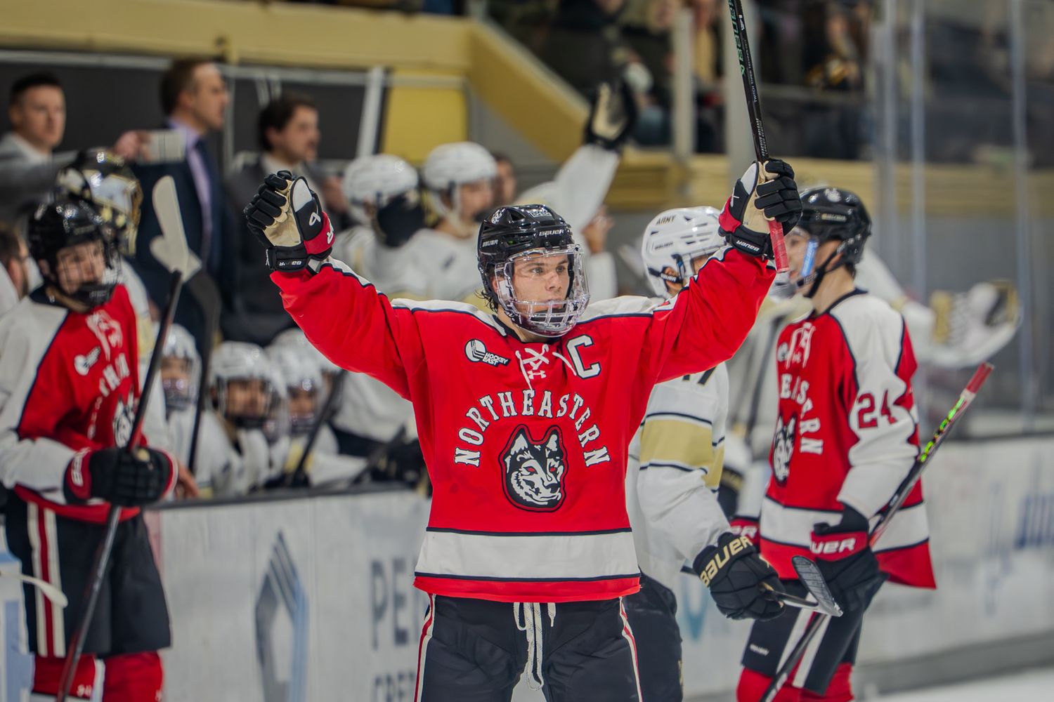 A hockey player in a red jersey celebrates with raised arms during a game while teammates look on.