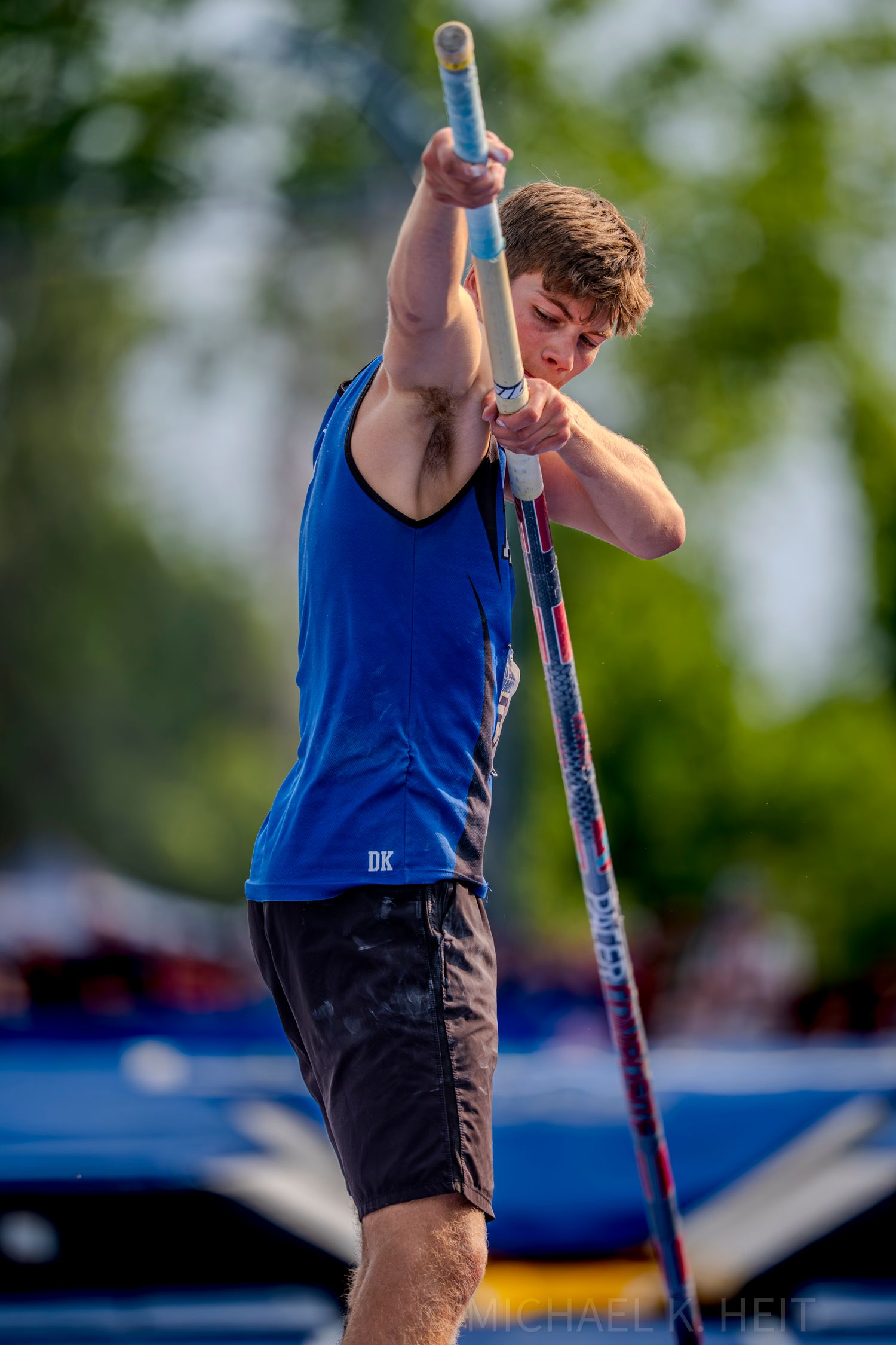 Pole vaulter executing jump sequence at outdoor track meet.
