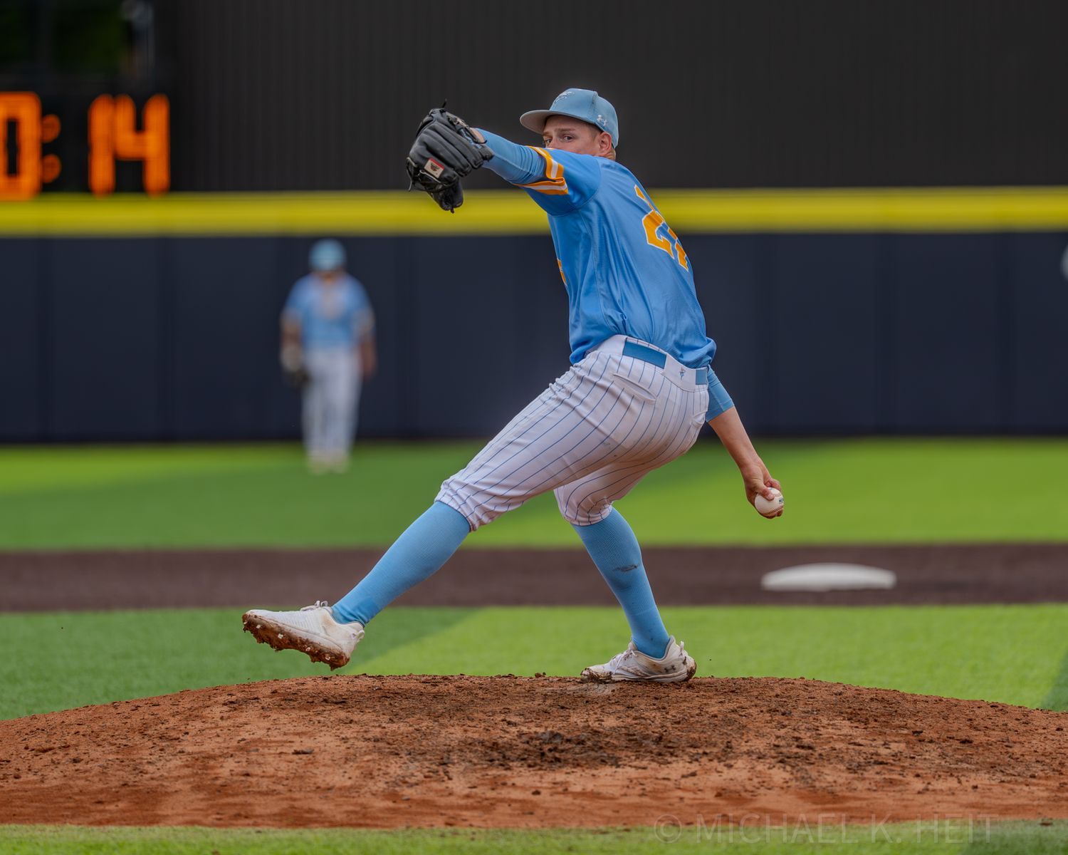 Baseball pitcher in light blue uniform mid-delivery on the mound during game action.