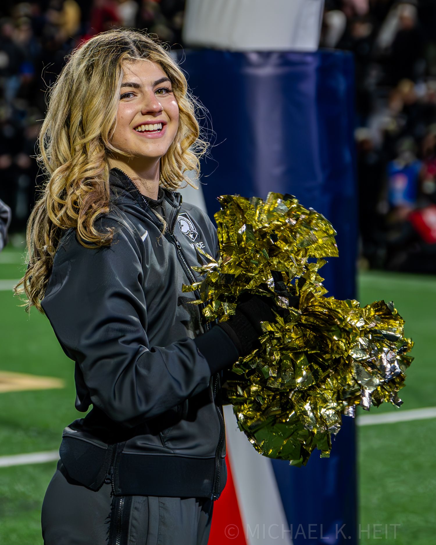 Cheerleader performs with gold pom poms during nighttime football game.