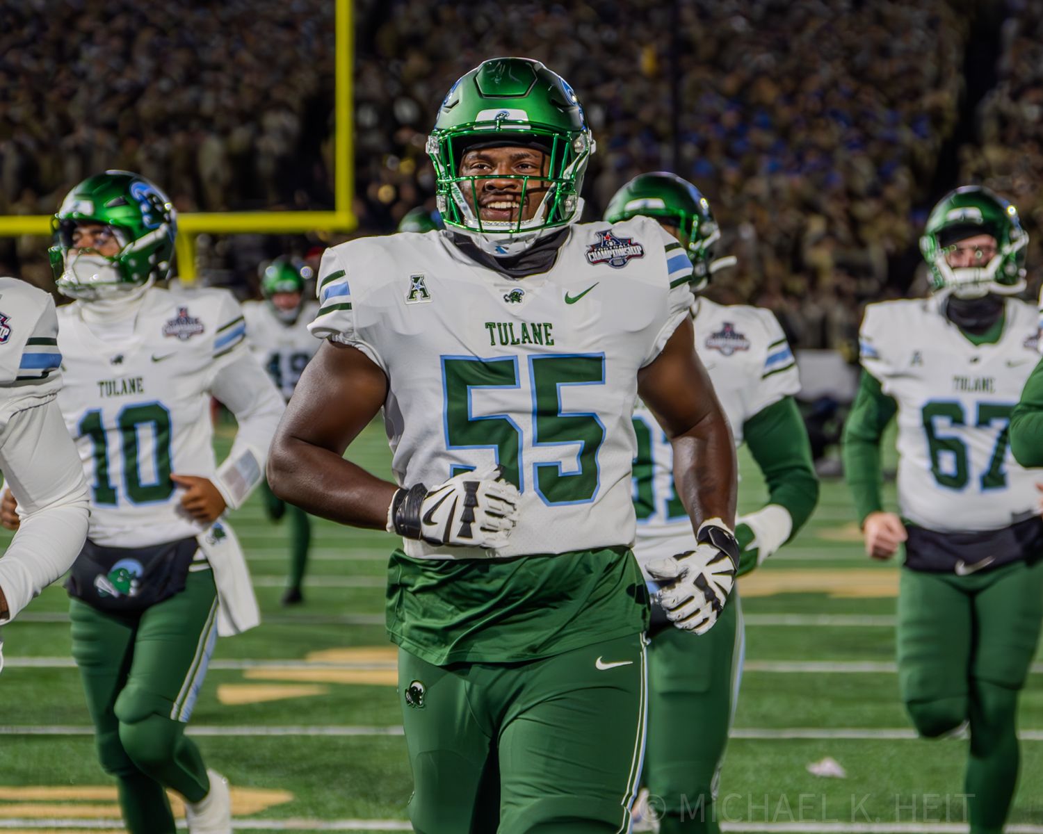 Players in green and white uniforms line up on football field during game.