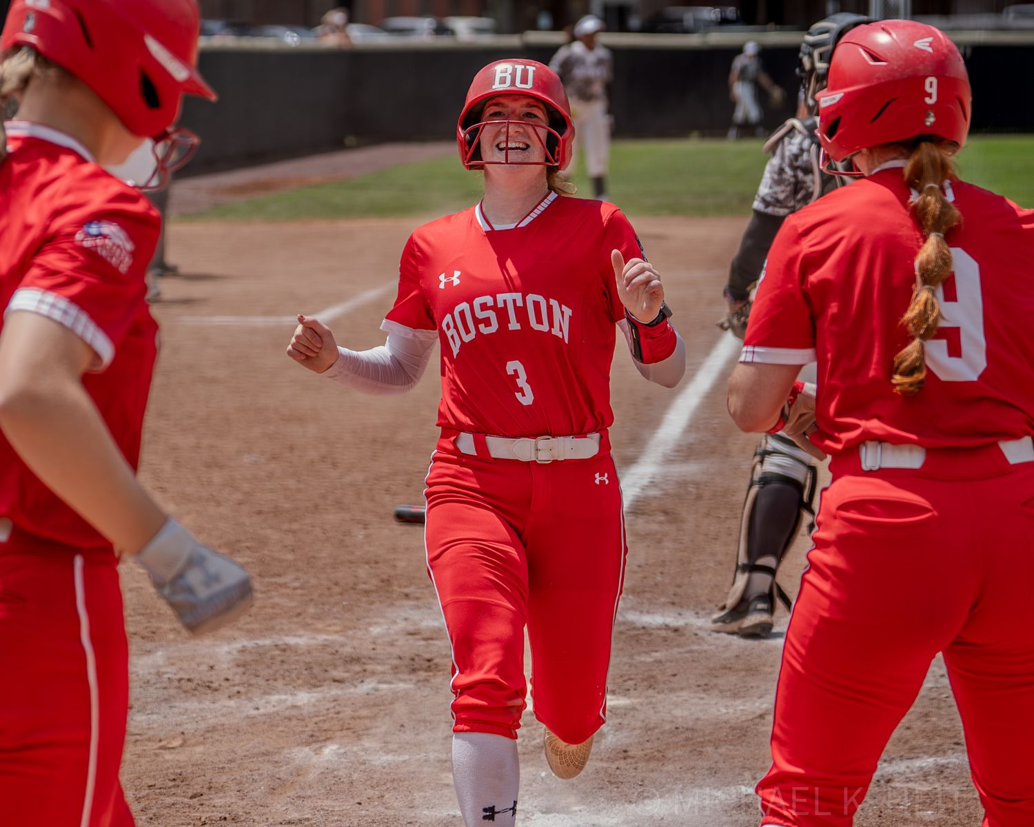 Team celebrating at home plate during softball game wearing red uniforms.