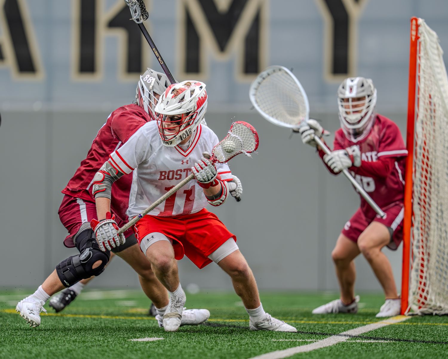 Collegiate lacrosse players compete near the goal during an intense match.