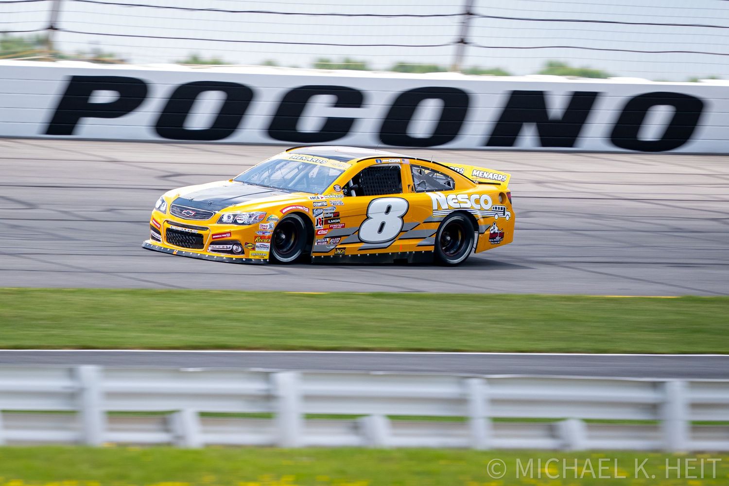 Yellow NASCAR #8 race car speeding on the Pocono Raceway track during a competitive race event.