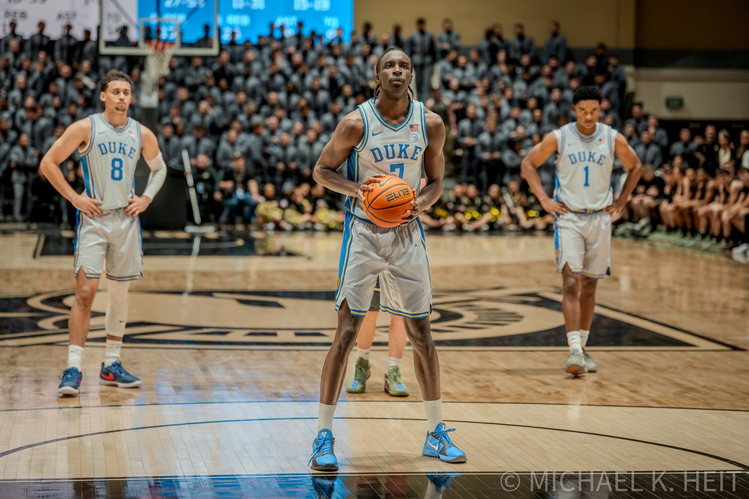 Basketball players in light and dark uniforms positioned on court during game play.