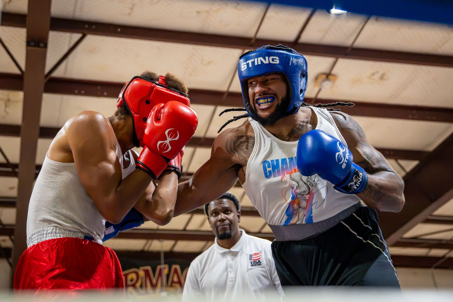 Two boxers sparring in a ring, one in red gloves and one in blue gloves, with a referee watching closely.